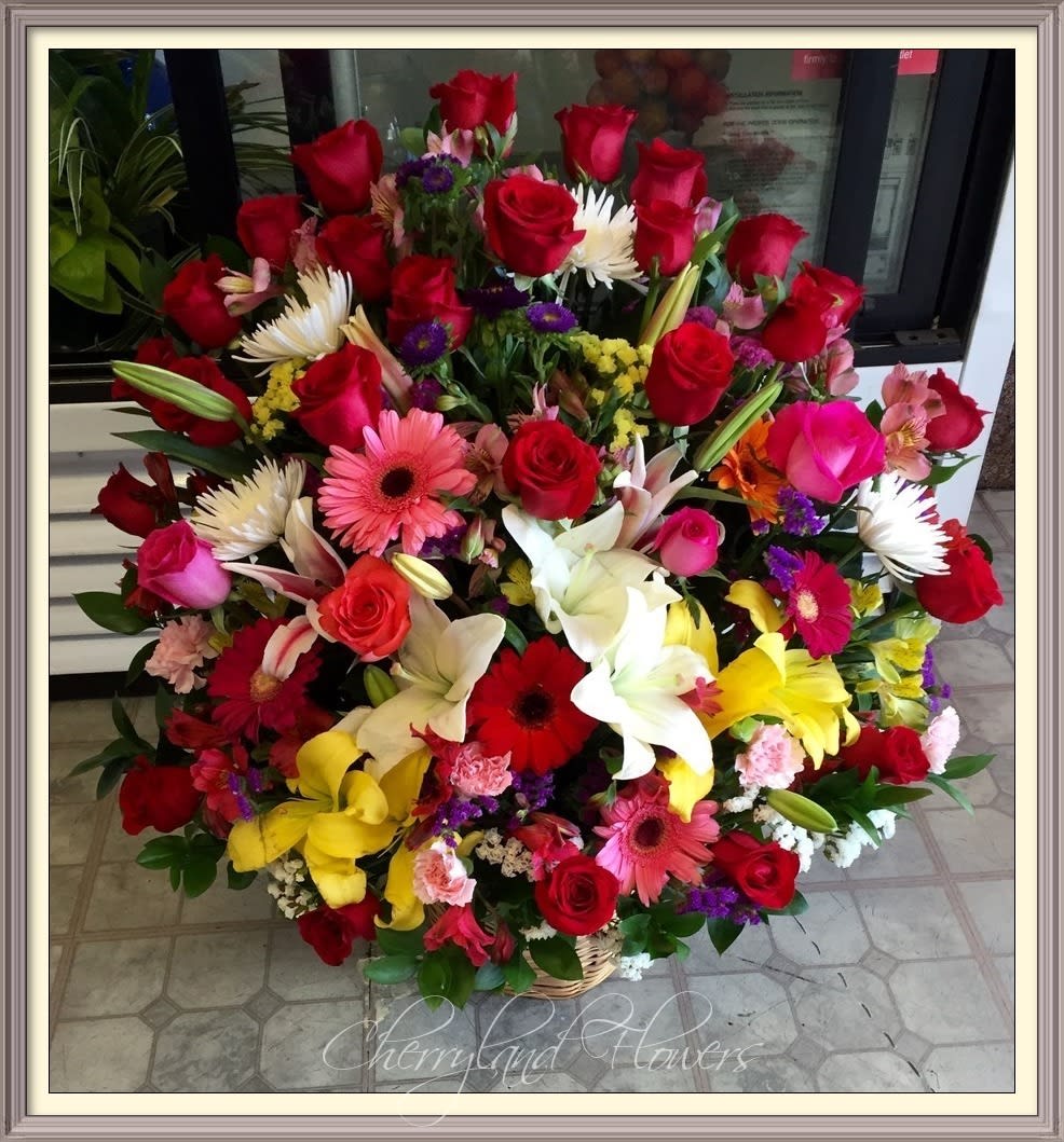 CF1052 - This floral masterpiece is sure to impress, featuring a lush assortment of red, pink, and orange roses, white spider mums, yellow and white lilies, pink carnations, pink, red, and orange gerberas, purple, yellow and white statice, pink alstroemerias, purple masumoto, and foliage artfully arranged in a grand basket. 