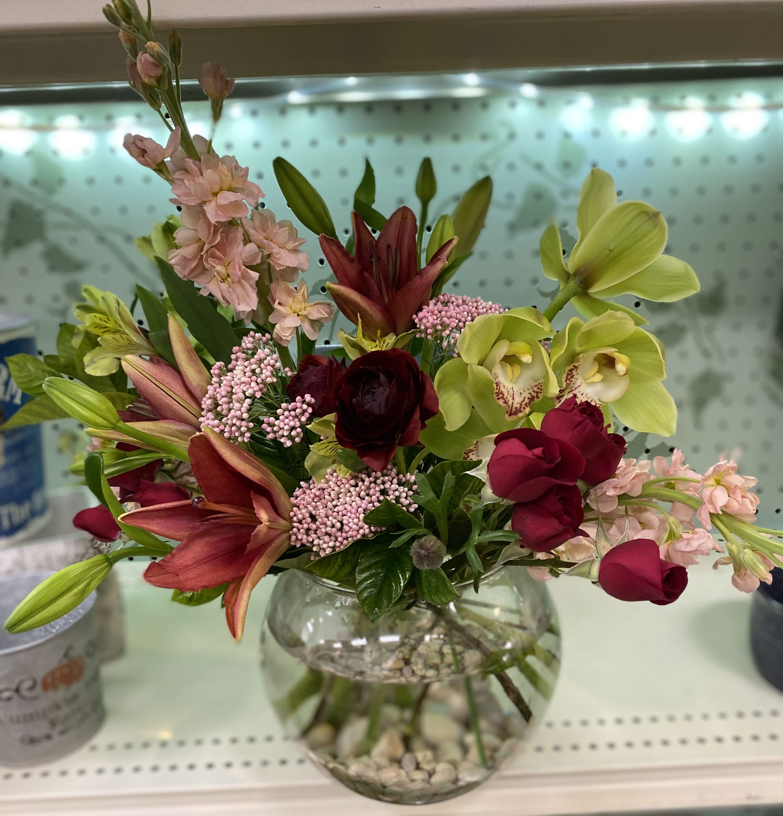 Red Lilly  - medium vase arrangement designed with with roses, lilies, orchids, stock, and spray rose in a bubble bowl. 