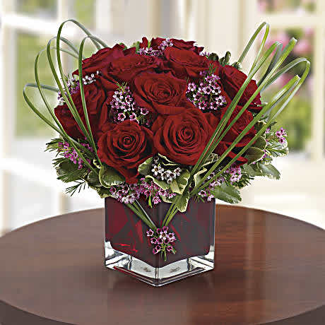Sweet Thoughts Bouquet with Red Roses Sweet Thoughts Bouquet with Red Roses - Send this premium version, and they'll know they've got your heart! With more roses - but the same classic, collectible cube vase in a shade of warmest crimson - this gift will be a surefire hit. A deluxe mix of red roses and purple waxflower - accented with bear grass and greenery - is delivered in a red glass vase.