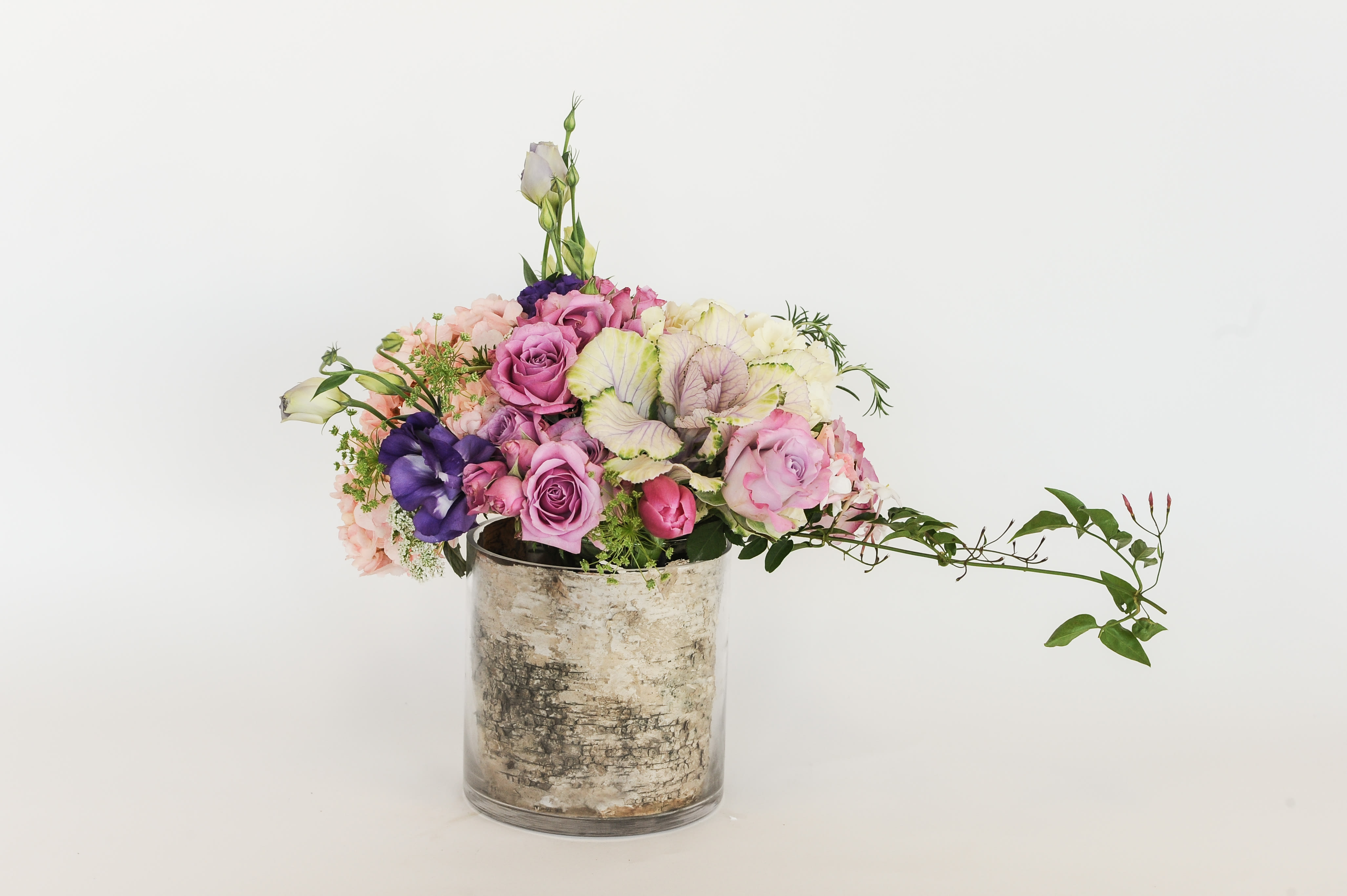 Rustic Arrangement Rustic Arrangement - Rustic spring arrangement with kale, roses, hydrangea, lisianthus, with jasmine vines in a beautiful glass vase (with ti leaves wrapped, instead of birchwood for long lasting flowers)