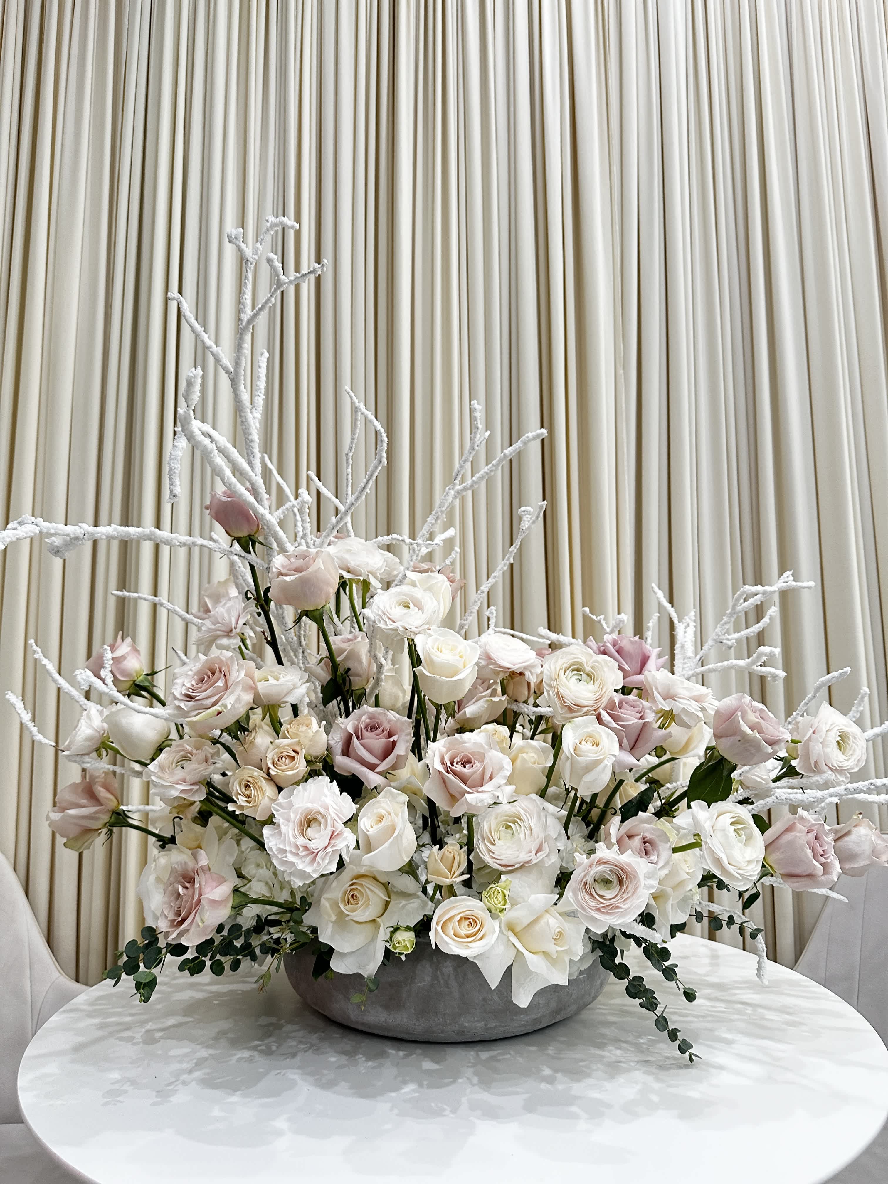 Winter Wonderland - Bring the magic of a winter wonderland indoors with this stunning arrangement. Featuring white roses, hydrangeas, and ranunculus accented with frosted birch branches, this arrangement is sure to add a touch of elegance and enchantment to your home.  