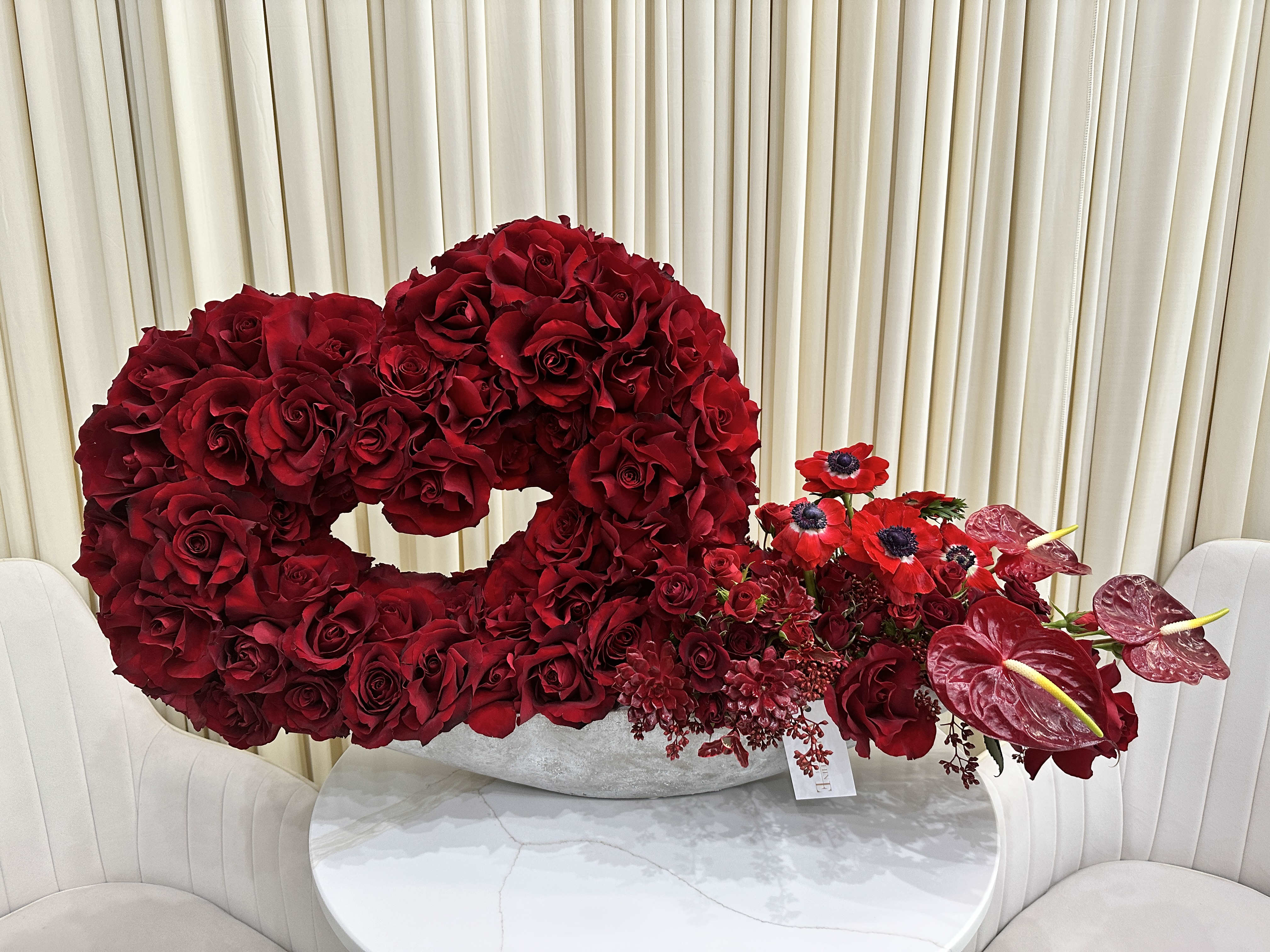Enchanting Heart - Capture Hearts with this Enchanting Red Rose Masterpiece  Let love bloom with this exquisite heart-shaped arrangement of premium red roses, handcrafted to express your deepest emotions. Each hand-selected rose boasts vibrant color and velvety texture, composing a romantic masterpiece sure to leave a lasting impression.  A Flourishing Expression of Love  This unique heart-shaped design transcends the ordinary, making it a one-of-a-kind expression of your affection. Imagine the delight on your loved one's face as they unveil this breathtaking display of love, its vibrant hues filling the room with a touch of magic.  More Than Just Flowers, a Work of Art  Our skilled florists are passionate artisans, meticulously hand-arranging each rose to create a visually stunning masterpiece. The perfect balance and placement of each bloom ensures that this arrangement is not just beautiful, but truly unforgettable.