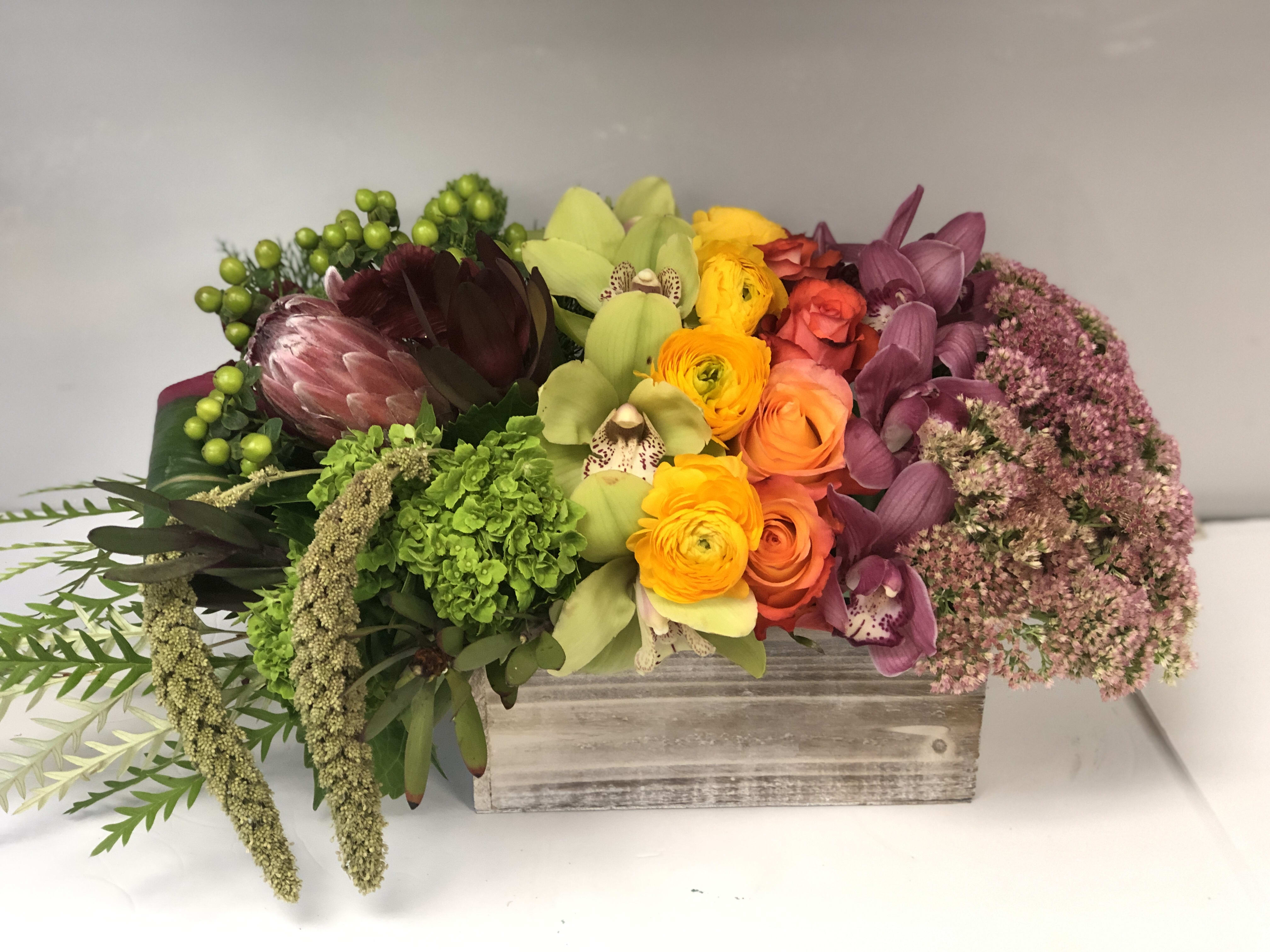 Art with tropical flowers  - Wooden rustic box with shades of colors of orchids ranunculus mini green hydrengeas and tropical flowers 