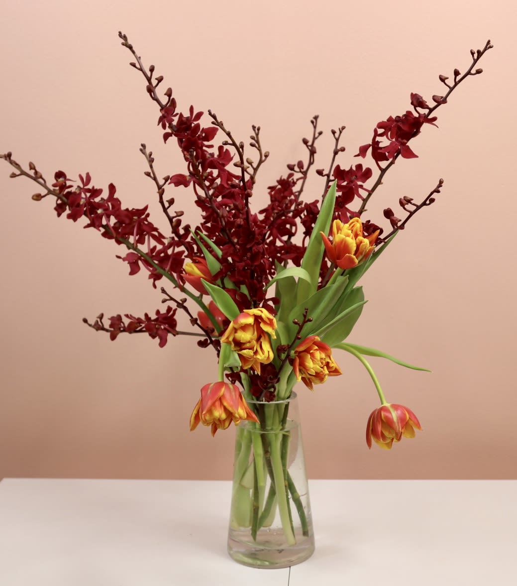 Eddie - Introducing Eddie! This bold and contemporary arrangement is expertly crafted in a 7-inch tall tapered vase, making it a stunning focal point for any modern space.  Key Features:  Modern Design: This arrangement showcases a sleek and modern design, perfectly complementing contemporary interiors with its clean lines and minimalistic aesthetic.  Tapered Vase: The 7-inch tall tapered vase adds a touch of chic elegance, enhancing the overall visual appeal of the arrangement.  Floral Dance: Immerse yourself in the dance of luxury as Renanthera orchids and gorgeous tulips intertwine in a harmonious display of color and form.  Why Choose Eddie:  Contemporary Chic: Elevate your home or office with a striking floral arrangement embodying contemporary chic's essence.  Premium Selection: The arrangement features the exquisite beauty of Renanthera orchids and tulips, selected for their opulence and lasting freshness.  Versatile Statement Piece: Whether placed on a dining table, console, or office desk, this arrangement makes a bold statement in any setting.  Perfect for:  Modern Interiors: Complement your modern living spaces with a touch of nature's beauty in a contemporary form.  Special Occasions: Gift this luxurious arrangement to celebrate milestones, birthdays, or achievements.  Corporate Gifting: Impress clients, colleagues, or business associates with a sophisticated floral gift that speaks volumes.