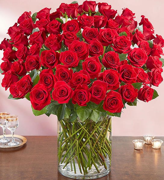 100 Fresh Premium Long Stem Red Roses - An arrangement with 100 premium long stem red roses; accented with assorted greenery in a clear big vase.