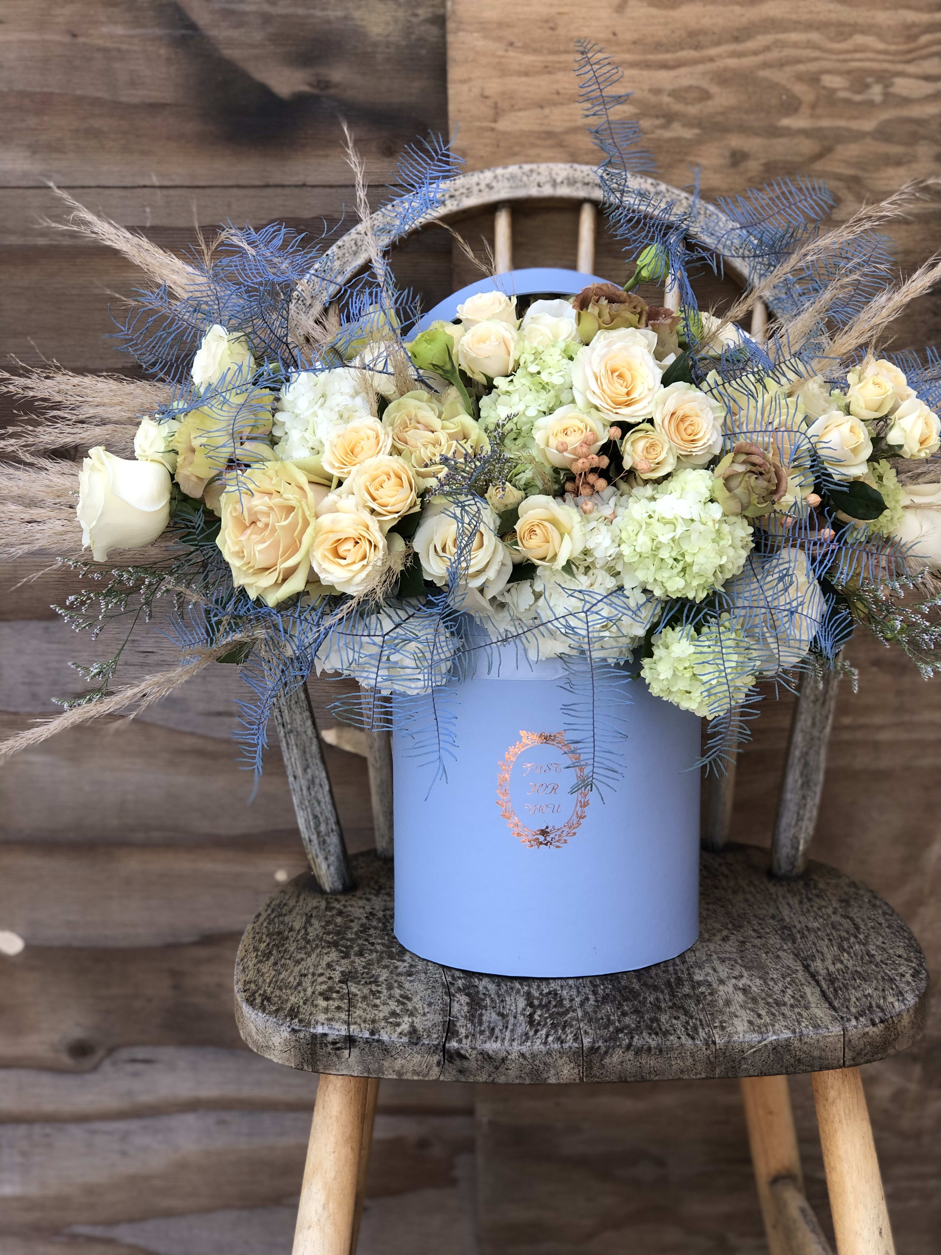 The Blue Box The Blue Box - Beautiful earthy tones arranged in blue box. Dried pampas grass and other dried flower accents are creative addition to fresh blooms of roses and hydrangeas. This arrangement can be created in all color pallets, just let us know your preference.