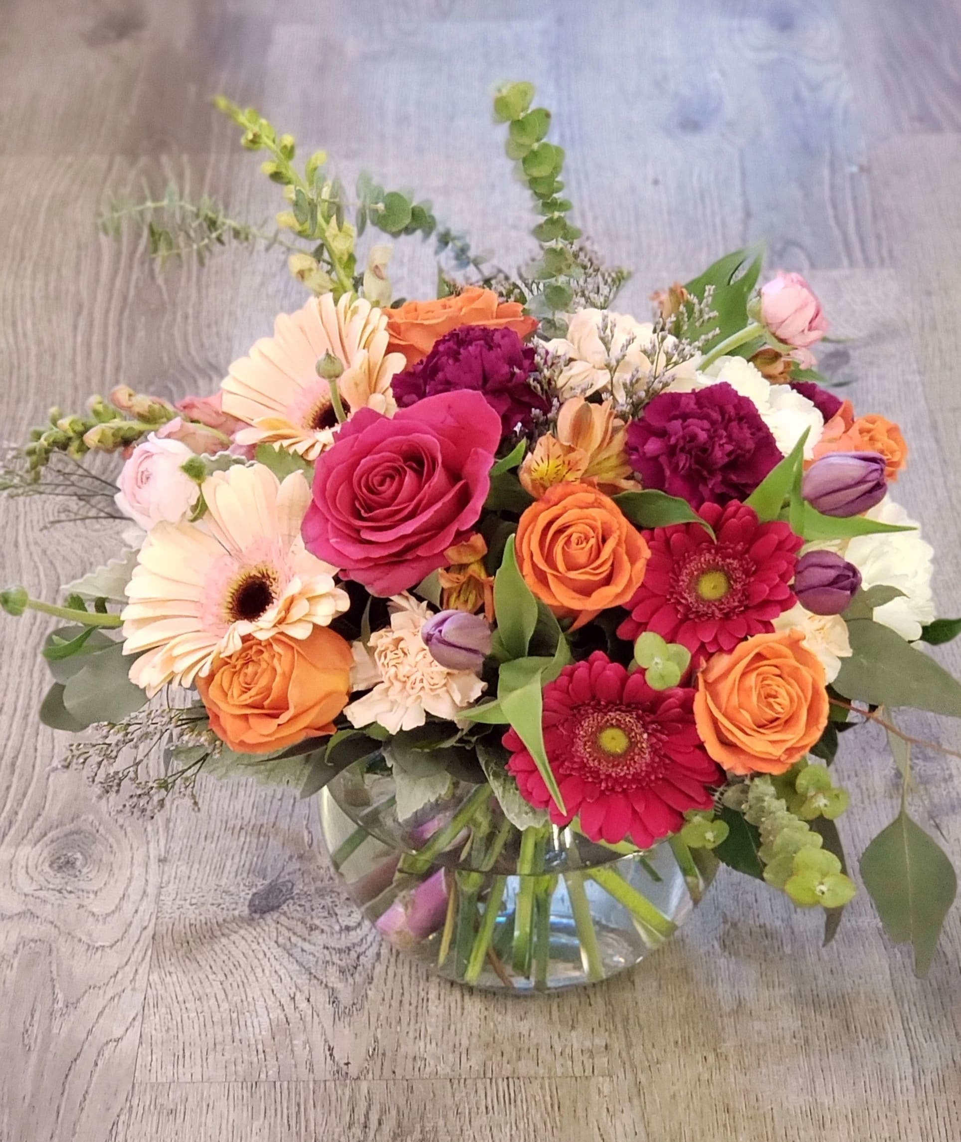 Seasonal MIX ARRANGEMENT  - A beautiful mix of seasonal flowers Rose's, ranunculus, kale, carnations, tulips, snap dragons, stock, Gerbera daisy wax flower,  baby eucalyptus, silver dollar eucalyptus,  dusty Miller Just gorgeous mix beautifully designed in a  clear vase bubble bowl or a clear cylinder vase or cube vase.  Pictured is premium Size  