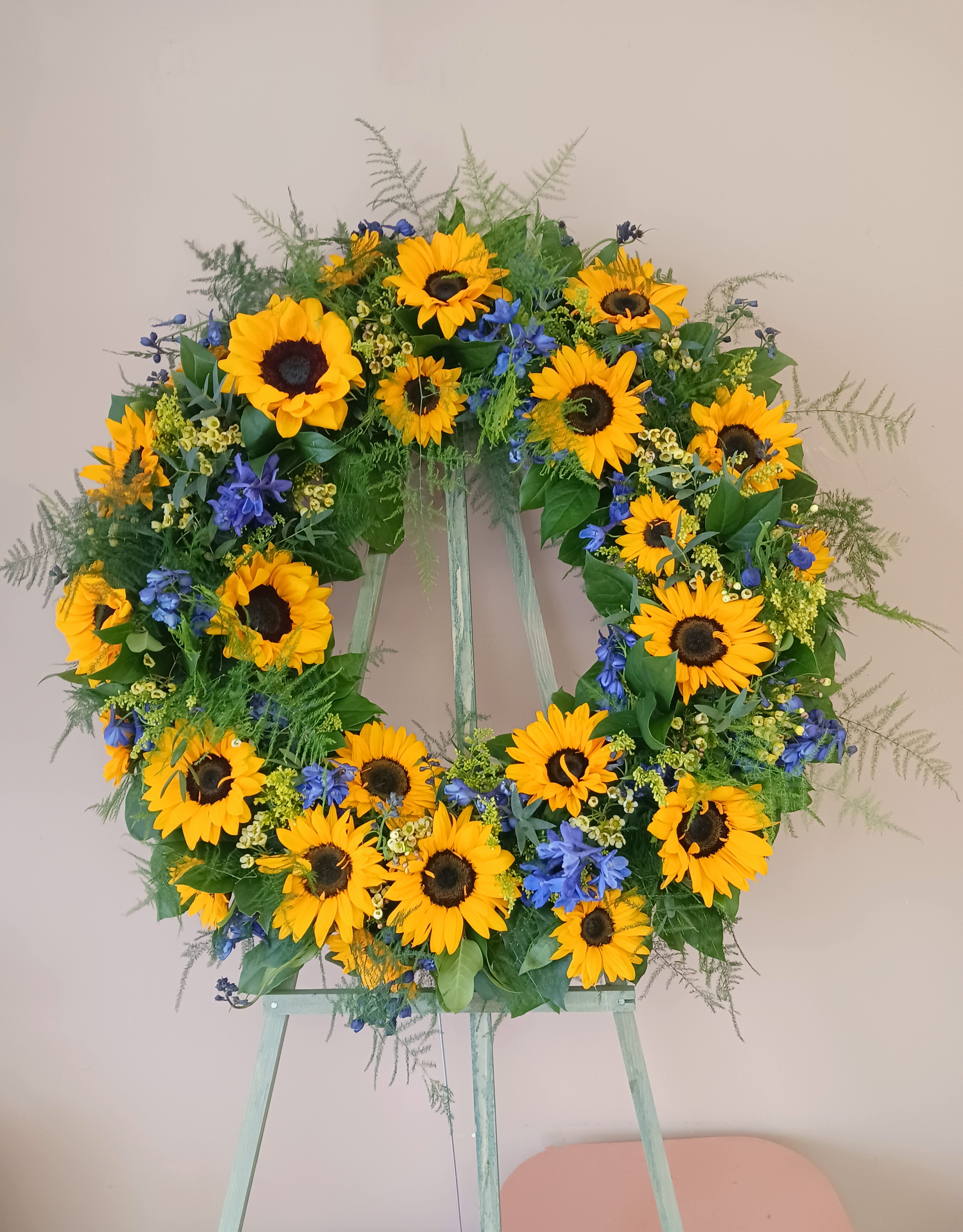 Sunflower Standing Wreath  - The wreath measures 21 inches in diameter. The flowers on the wreath are sunflowers, blue delphinium, wax, solidago and foliage. (Easel is included) 