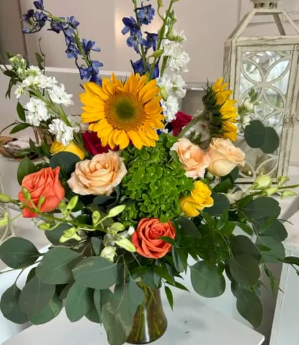 Sunshine Medley Sunshine Medley - A bright and cheerful floral arrangement, composed of a variety of flowers that create a lively and inviting display. The centerpiece of the bouquet is a bold sunflower, its large, open face and sunny yellow petals standing out as a symbol of happiness and warmth.