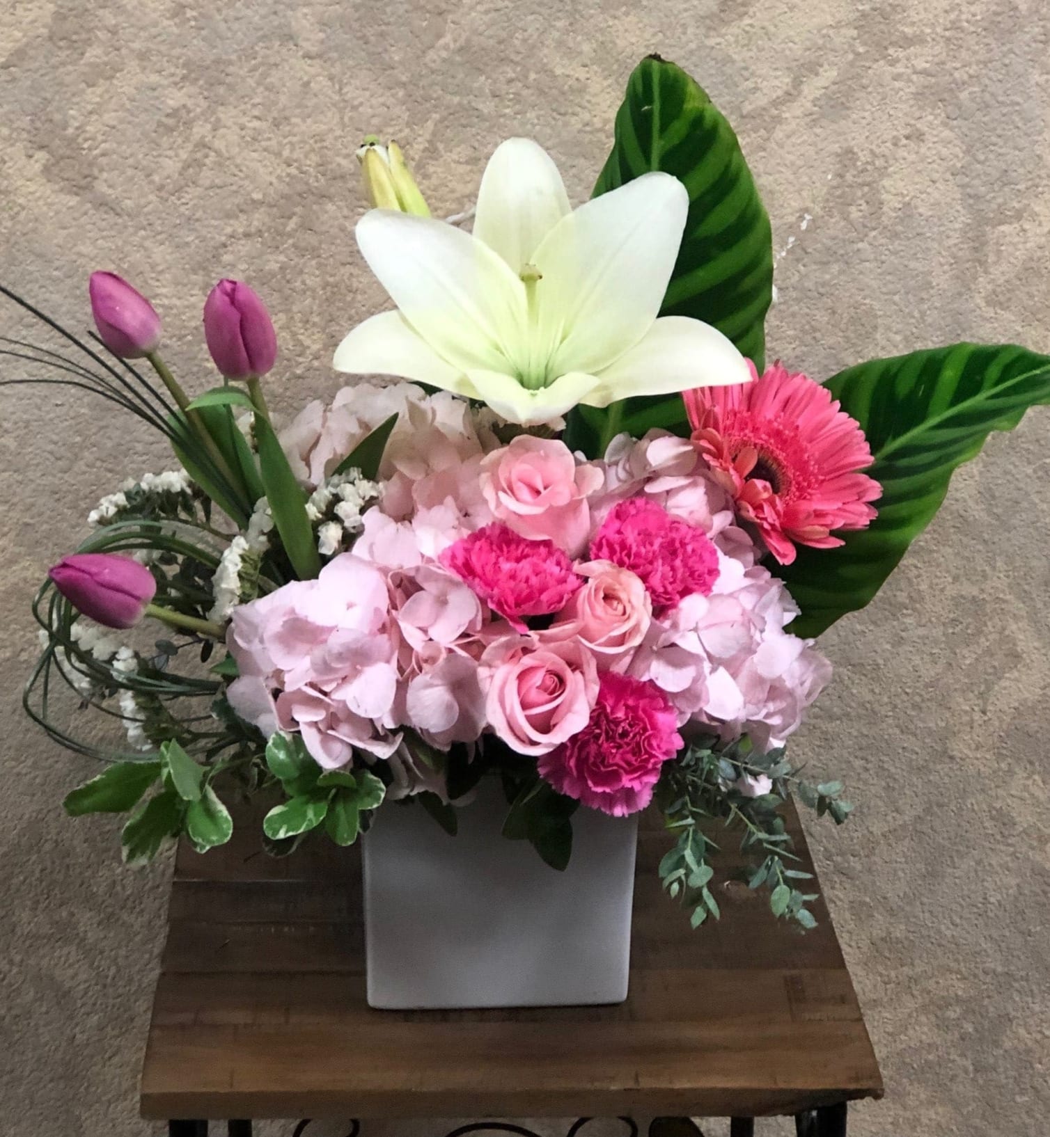 Santorini, Greece - Type of Flowers: White Lilies, Pink and White Hydrangeas, Pink Roses, Pink Gerberas, Pink Carnations, Purple Tulips and more in a square white vase. Availability: All year round Substitute Available: Yes Design View: Symmetric Front Facing View Photo shown: Regular