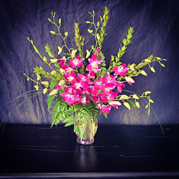 Bombay Orchids - This simple yet elegant design features lush purple Bombay dendrobium orchids enhanced with lily grass and presented in a small vase.  Perfect for someone's desk!
