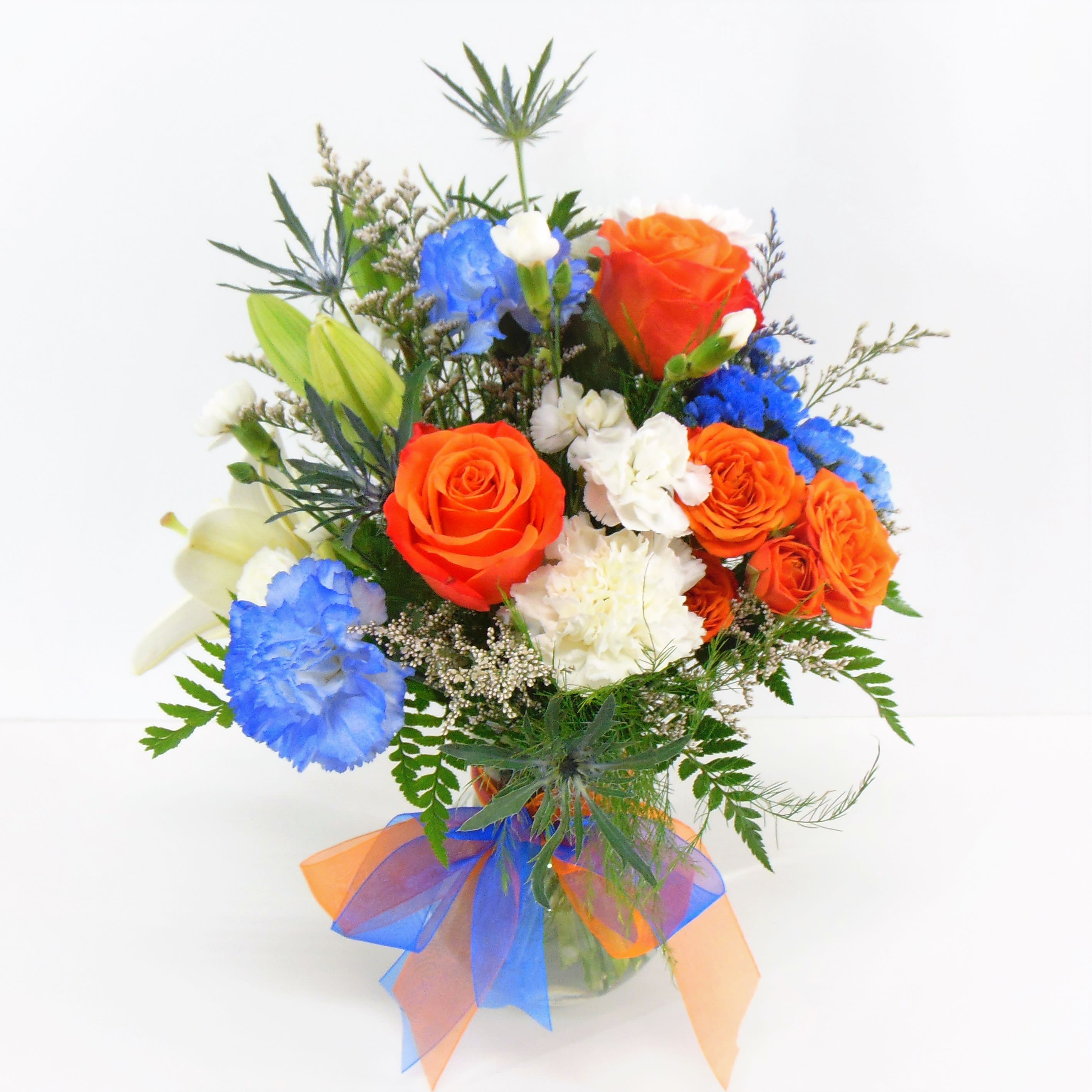 Bulldog Spirit in Orange &amp; Blue - Send celebration wishes with this colorful bouquet of school spirit and blooms of lilies, carnations, blue thistle and roses. Designed one-sided in a glass vase and the deluxe option is pictured.