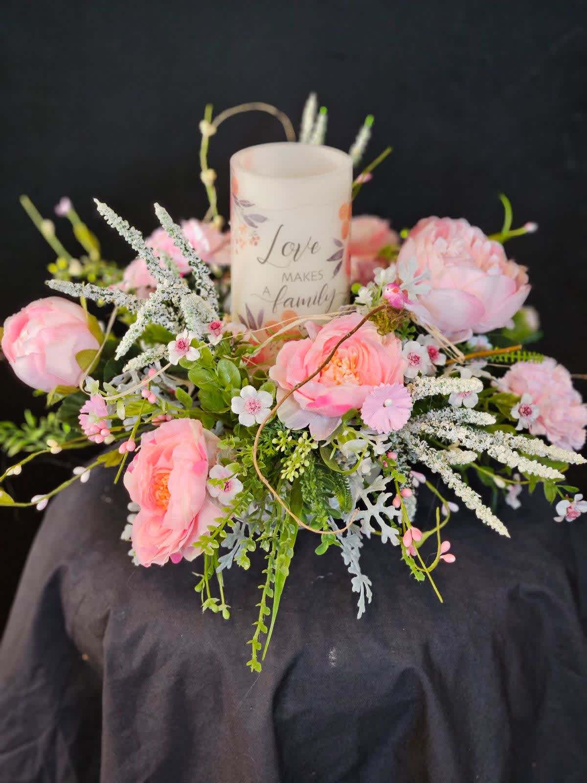 Eckert Florist's Love Makes A Family Bouquet - This artificial arrangement includes a battery operated candle inscribed with &quot;Love Makes A Family&quot;. Designed with artificial Roses, Peonies, and Carnations this arrangement will make a wonderful centerpiece for any family member. *our local delivery only   *Our local delivery only 