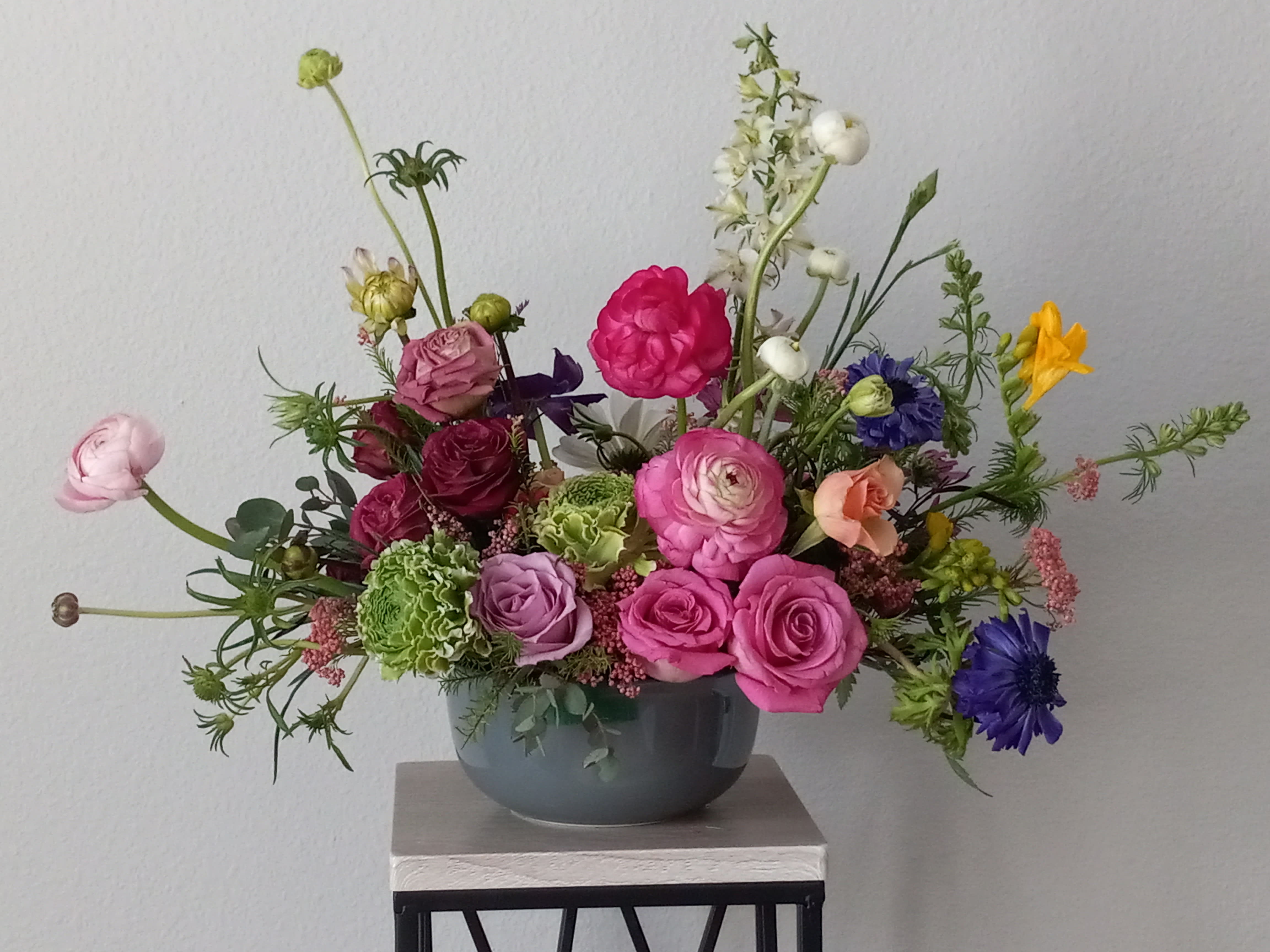 Blush Life Blush Life - Put a spring in their step with this beautifully blushing bouquet of hot pink, pink and green ranunculus, hot pink roses, yellow freesia, purpule anemone, burgundy lisuanthus, greeneries. it's a chic treat for any occasion! Delivered in a gray gathering vase. Orientation: All-Around SUBSTITUTION POLICY – Always deliver the freshest flowers! Please note the bouquet pictured reflects our original design. If the exact flowers or container in this arrangement are not available, our local florists will create a beautiful bouquet with the freshest available flowers.