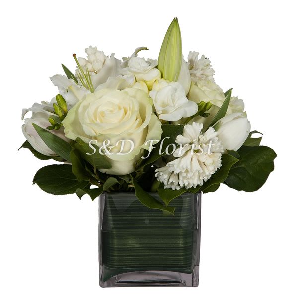 Classy Lady - In a 6&quot;  glass cube lined with ti leaf creating an elegant arrangement of a selection of white flowers to fit any occasion. Provides a nice feel and scent of purity with a texture, consisting of all white flowers as: lilies, lisianthus, snap dragon, freesia, tulips, roses, gerbera, daisy, hyacinth, spiced up with a touch of princess pine.  Dimensions:11&quot;H x 8&quot;L