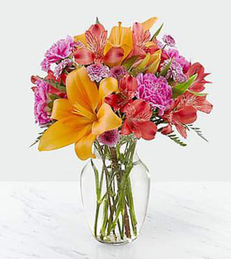 Light of My Light Bouquet Light of My Light Bouquet - Fuchsia Carnations, Red Alstroemeria, Lavender Buttons, and Orange Lily's with greens in a clear vase.