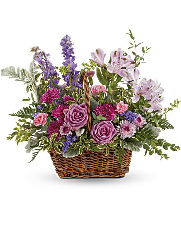 Lavender Meadow Bouquet - This lush lavender rose arrangement is a basket of beauty to brighten any day! This bouquet features lavender roses, lavender alstroemeria, miniature pink carnations, lavender larkspur, purple cushion spray chrysanthemums, lavender button spray chrysanthemums, purple sinuata statice, dusty miller, pitta negra, parvifolia eucalyptus, lemon leaf and leatherleaf fern. Delivered in a Rectangular Basket with Handle. Orientation: One-Sided 