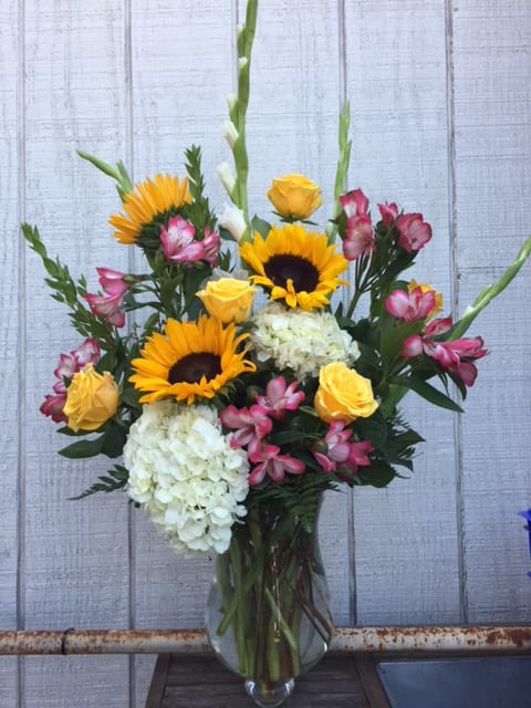 Sweet Spring Bouquet - A lovely one sided arrangement with sunny sunflowers, hydrangeas, roses, alstroemeria, and gladiola flowers. This is one of our designs so we may not have the exact same flowers or vase. 