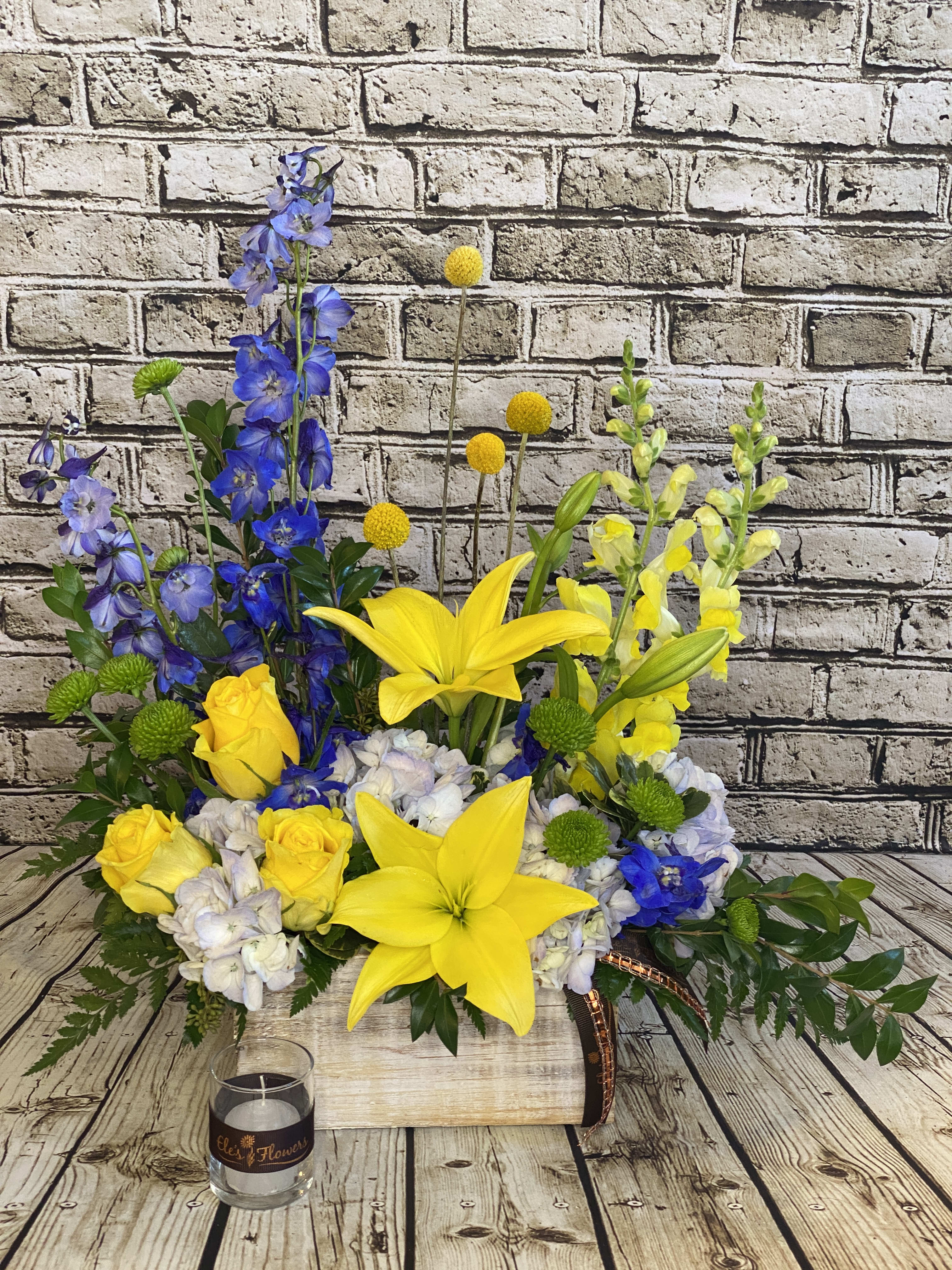Blue, White, Yellow Remembrance Arrangement  - A lovely assortment of blues, yellows and white. Our design has a wildflower like appearance. The designs we create are custom and the blooms and containers will vary. We use the freshest product available to create the perfect floral combination for the recipient! If you have any special requests, please add those in the &quot;special instructions&quot; portion of your order to help us dial in your vision. Otherwise, our skilled designers, Brett &amp; Sara, will take it from here! Please note that the photos are examples only – floral selection will vary but colors will remain the same.   Approx. Dimensions: 20”+H x 16”+W