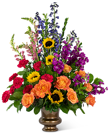 Prismatic Rays Grande Tribute - Send a bouquet that reminds them of the bright spirit of their loved one. The Prismatic Rays Grande Tribute represents the strength and beauty of the person you are honoring. Carnations, Snapdragons, Stock, Delphinium, Sunflowers, Roses and Myrtle are arranged in a bronze vase. 