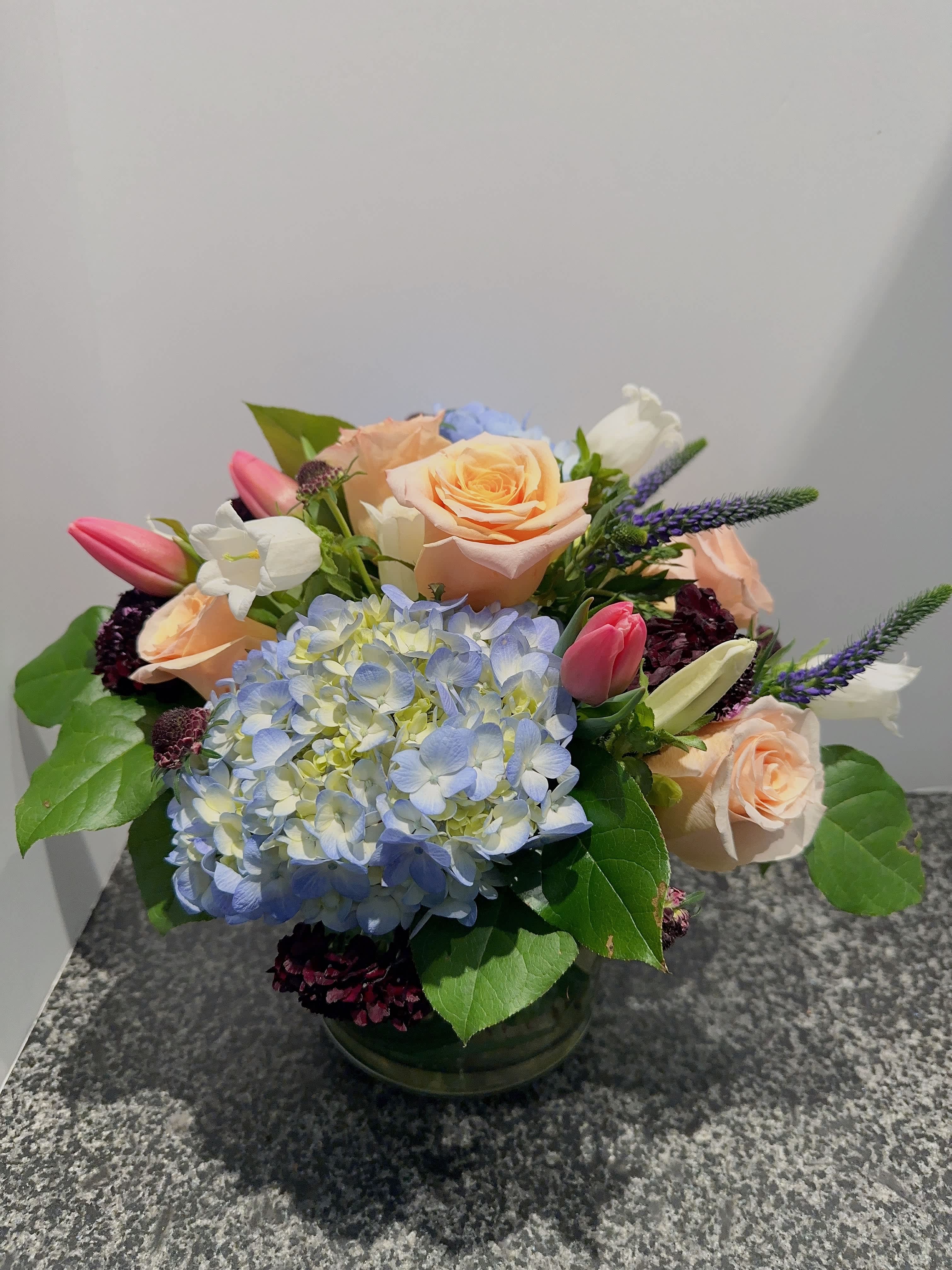 Wake Up Spring - This arrangement features warm and bright spring color. The arrangement include blue hydrangea, peach color roses and burgundy scabiosa. It is presented in a 6&quot; cylinder glass. 