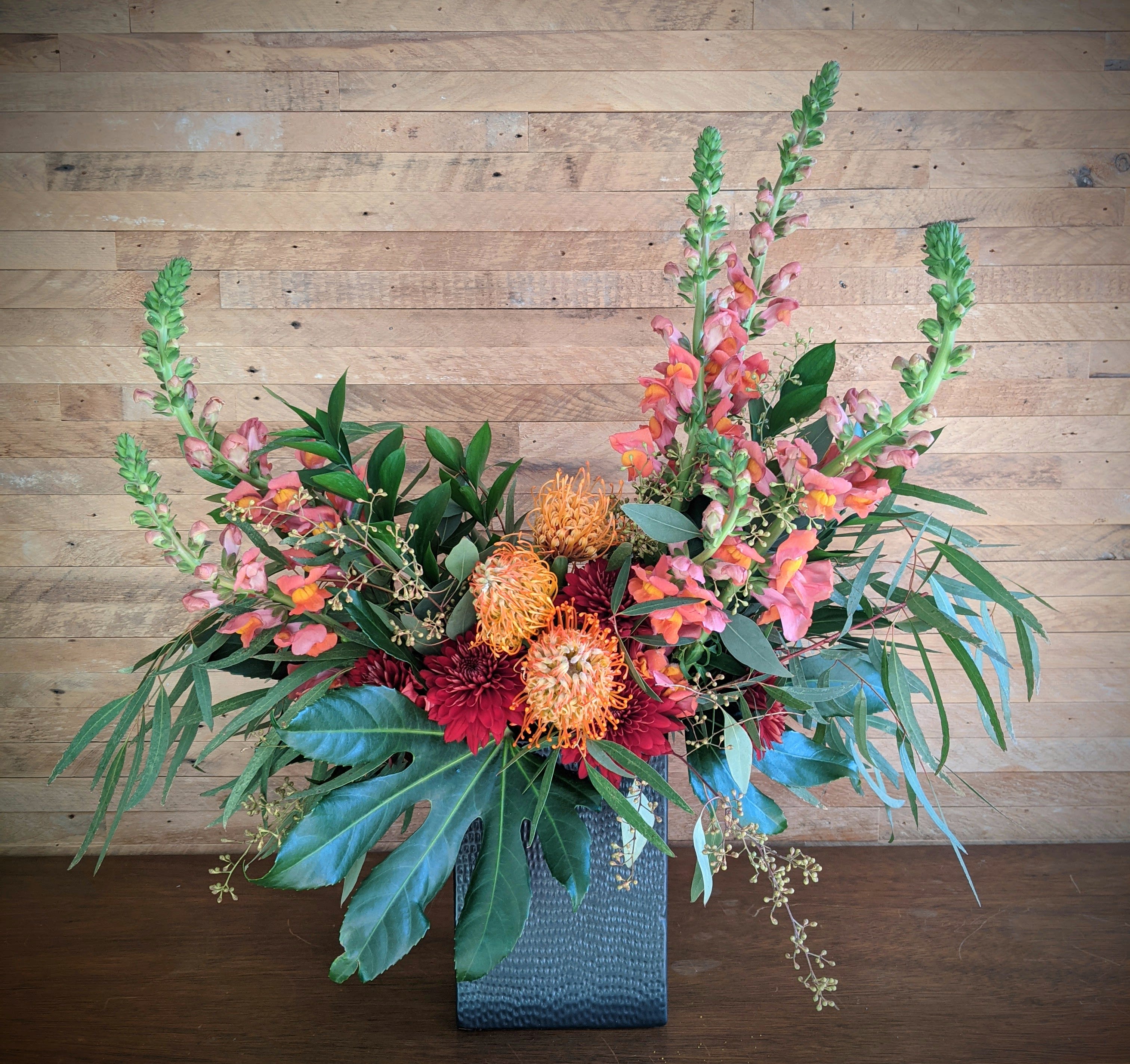 The Staples Mill The Staples Mill - A beautiful mix of lush tropical and forest foliage, pincushion Protea, Cremons, and snapdragons in a modern black ceramic container. Approx 24" tall and 20" wide. Hand-arranged and presented in a ceramic container. The image shown is an indication of our signature Studio Louise Flowers design style. We will create an arrangement featuring the best of the season in a similar style and color palette. Flowers are subject to seasonal availability. In the event that any of the flowers are not available, we will substitute them with a similar flower in the same shape, style and color. Standard size pictured. Stem count, container and packaging may vary. The container shown measures approx. 10 inches tall. Flower delivery to Stillwater and St Croix Valley.