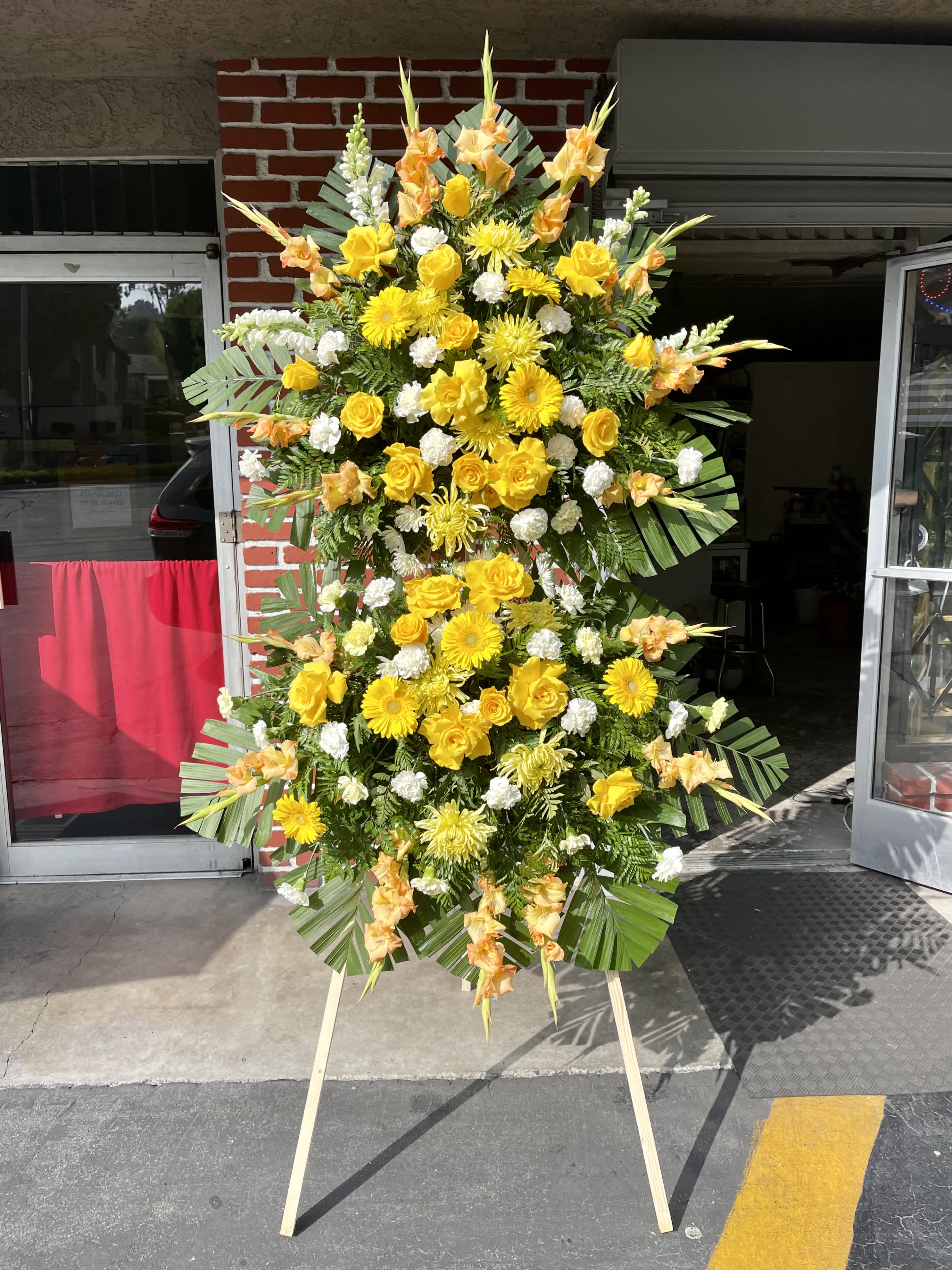 Korean Traditional Double Sympathy Standing Spray- Yellow - Show support for your loved ones with this vibrant yellow standing spray. The long, customizable banners allow you to both send your message of comfort, and easily let your loved ones know who is supporting them. The banners are carefully placed so that both the beauty of the flowers and the warmth of your heart shine through. This stunning arrangement includes a yellow and white variety of roses, gerbera daisies, gladioli, chrysanthemums, carnations, and snapdragons with a backdrop of commodore and other greenery. To make the arrangement as fresh as possible, flower colors and varieties may vary based on seasonal availability. Please leave your banner messages (left and right) in the special instructions upon ordering.