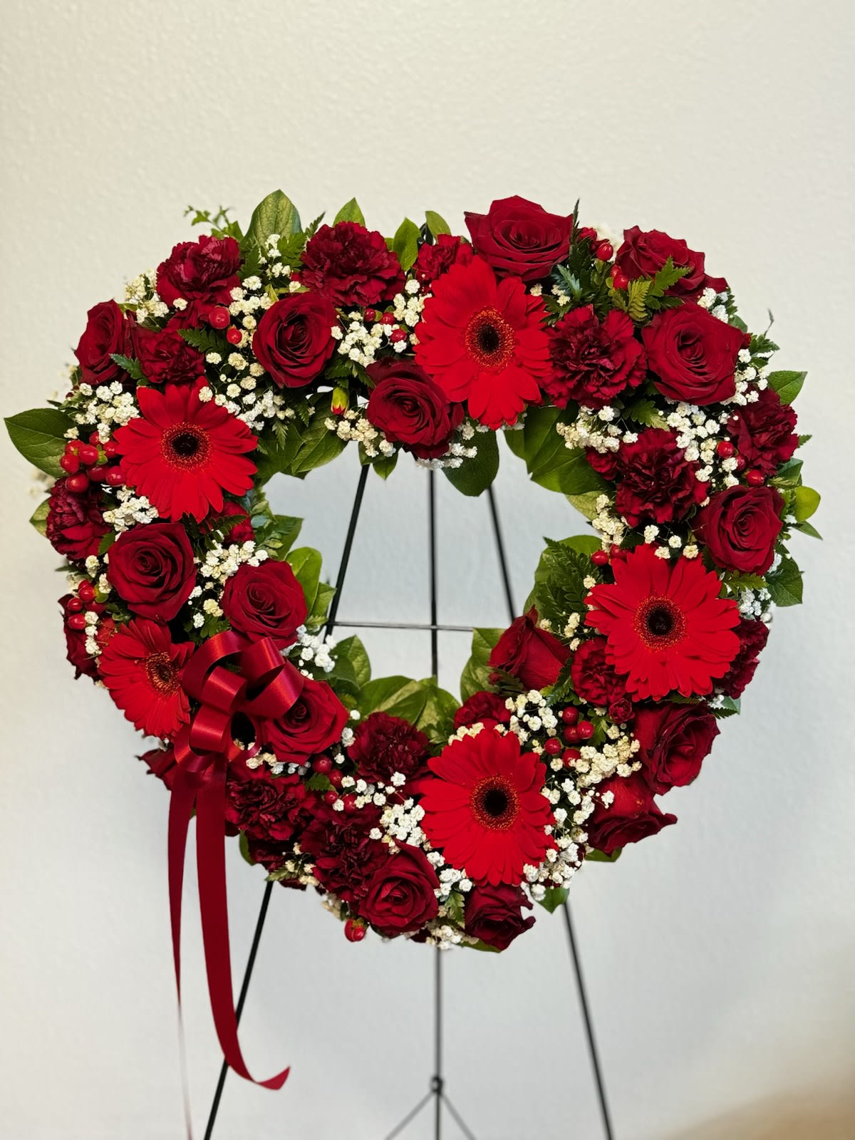 Heartfelt Sympathy Spray - Our Heartfelt Sympathy Spray is a touching tribute to express your deepest condolences to a loved one who has passed on. This magnificent standing spray includes a beautiful combination of red flowers, including gerberas, roses, and carnations, brought together to create a symbol of love, devotion, and honor. A red ribbon beautifully, adding an extra touch of elegance and reverence.  The red gerberas are symbolic of cheerfulness and joy, while the roses represent respect and deep love. The red carnations evoke emotions of sincere love, affection, and remembrance. The choice of red flowers symbolizes the strength of our emotions, and the ties of love that bind us to those we have lost.  The Heartfelt Sympathy Spray is a beautiful way of expressing your innermost thoughts and feelings of love for someone who will always hold a special place in your heart. It is a touching representation of the bond that will never be broken.  Order the Heartfelt Sympathy Spray to express your love and remembrance to those who have passed on. Let this beautiful standing spray be a source of comfort and solace to you and your loved ones during this difficult time.