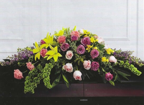 Forever Beloved Casket Spray - 14&quot;H x 30&quot;W x 43&quot;L Deluxe (CS10-1D) $365 (pictured) Premium (CS10-1P) $495 Casket spray of lavender roses, pink roses, lavender larkspur, pink carnations, Bells of Ireland, yellow Asiatic lilies and yellow freesia.