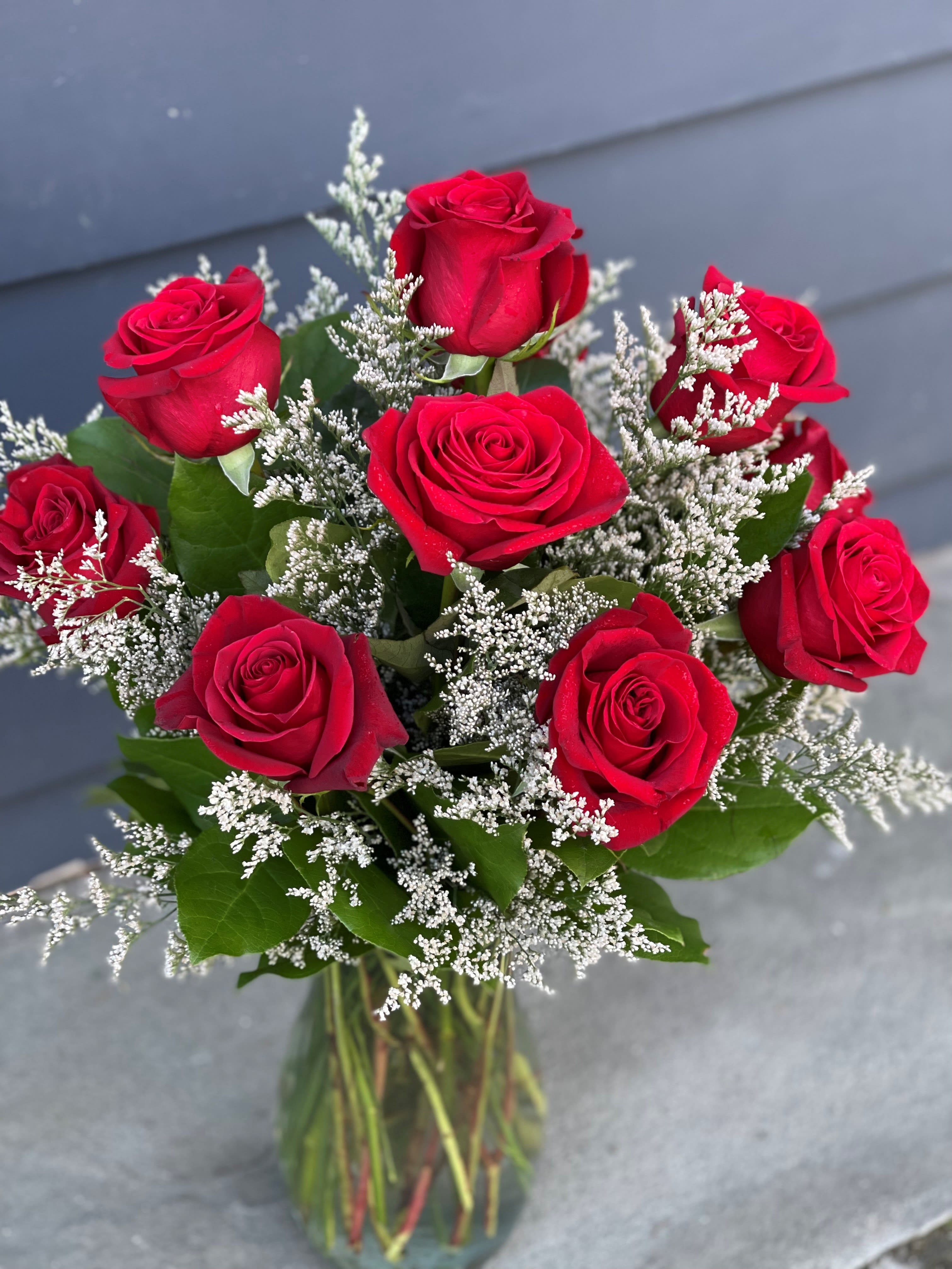 Premium Dozen Red Roses - 12 Premium long stem red roses artfully arranged in a recycled clear glass vase with greens and seasonal filler.