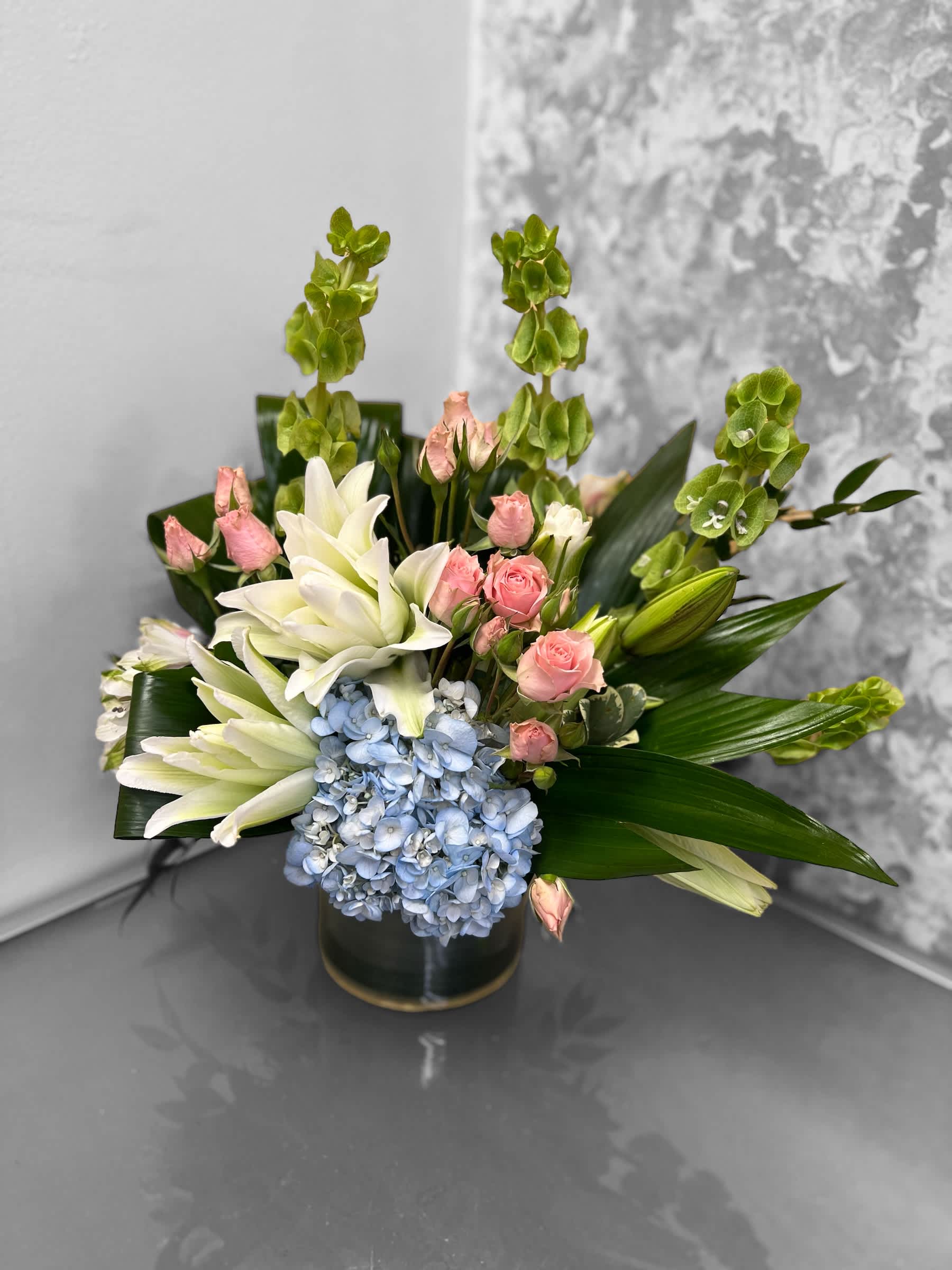 Athena  - This beautiful arrangement is a wise choice to give anyone for any occasion. Designed in a cylinder vase with hydrangeas, lilies, sweet roses and luscious greens. 