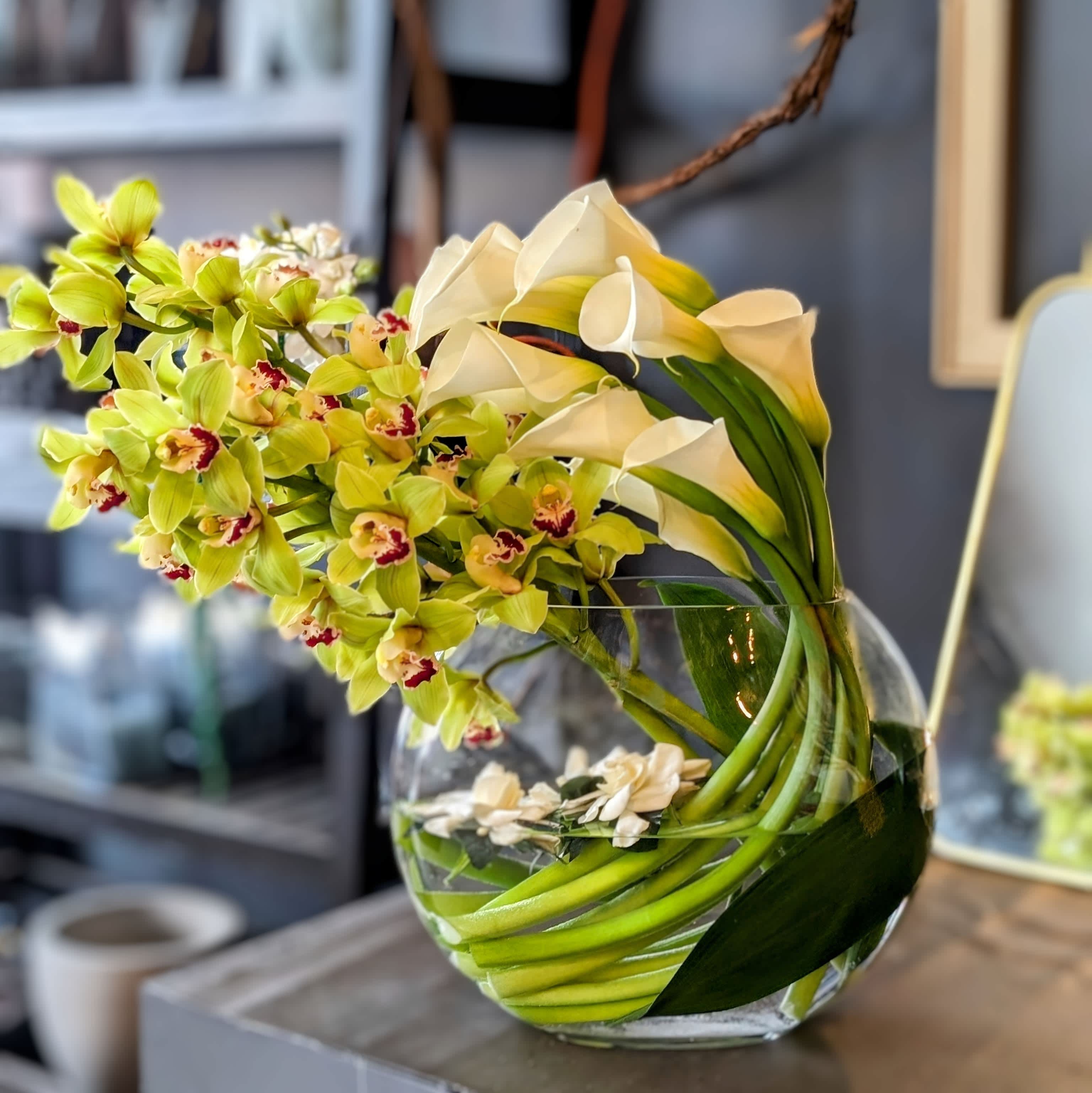 Magnificent Calla Lillies, Green Cymbidium orchids and floating Gardenias Magnificent Calla Lillies, Green Cymbidium orchids and floating Gardenias - This design is huge and quite impressive, with our huge moon vase is filled with the sweet scent of fresh cut gardenias. \