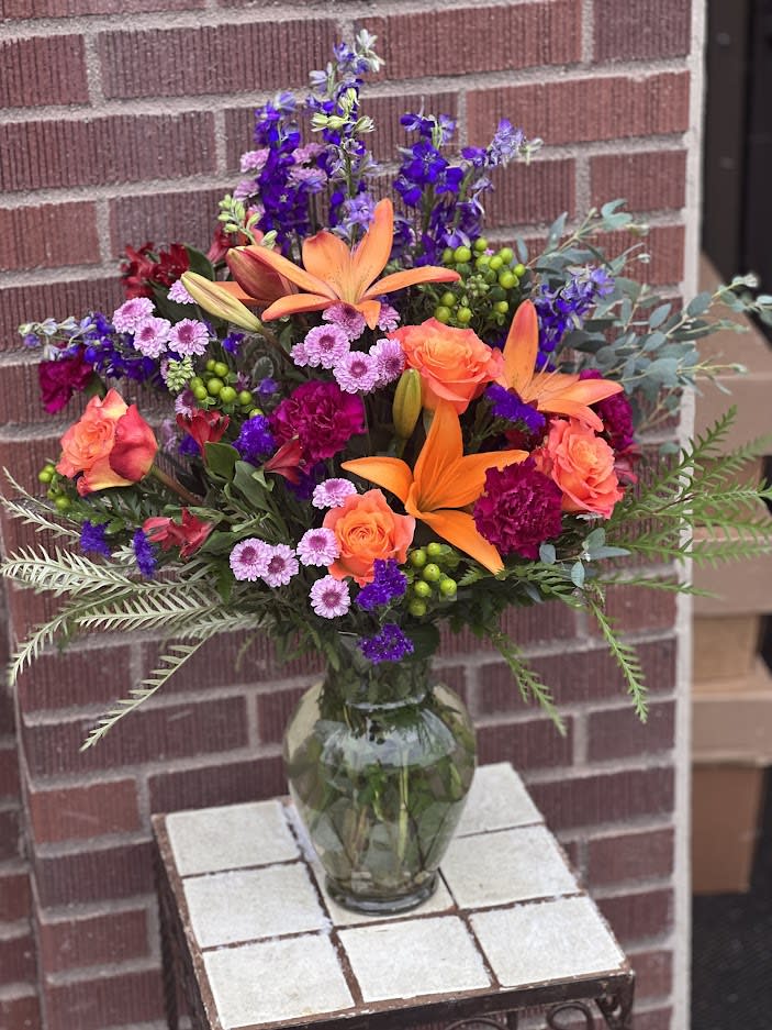 Signature Piece Signature Piece - In a beautiful vase that shifts from purple to clear on its way up, this orange and purple arrangement includes Asiatic lilies (no scent!), "Free Spirit" roses, button poms, larkspur, snapdragons and alstromeria lilies. Product ID: sigpiece