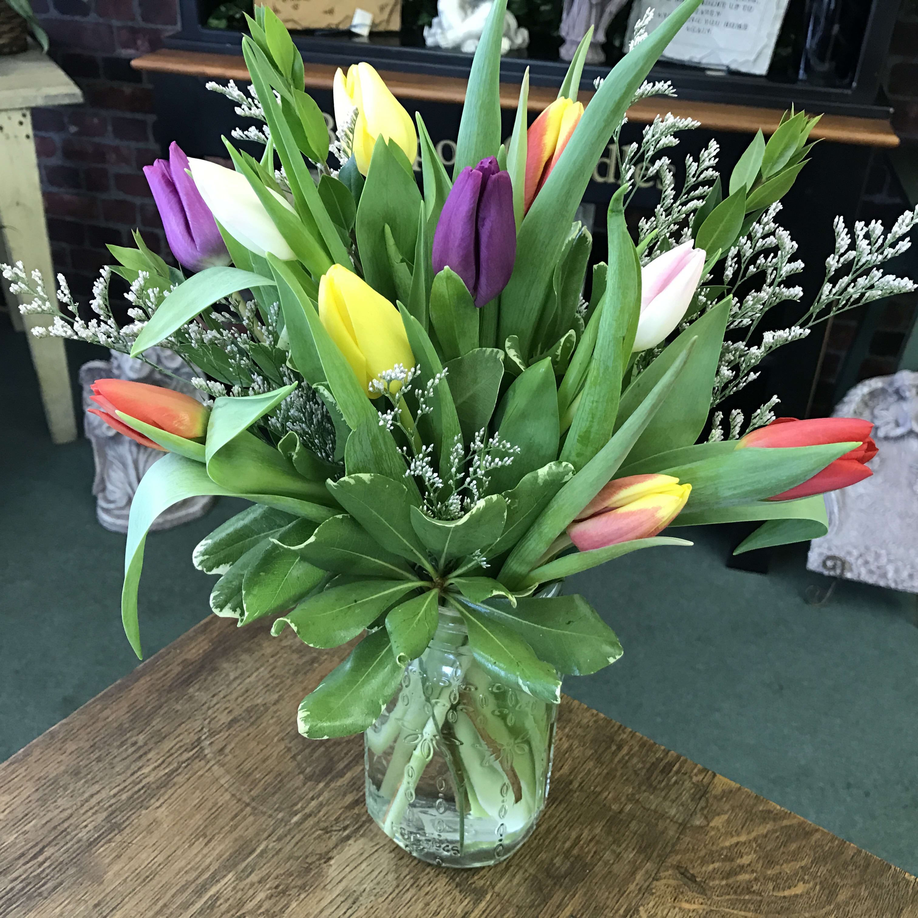 Spring Tulips - 10 assorted colored tulips along  with lush greens and filler are designed into this clear vase. A sure sign of spring! ** Tulip colors will vary as we are constantly getting in different colors from our farms.**