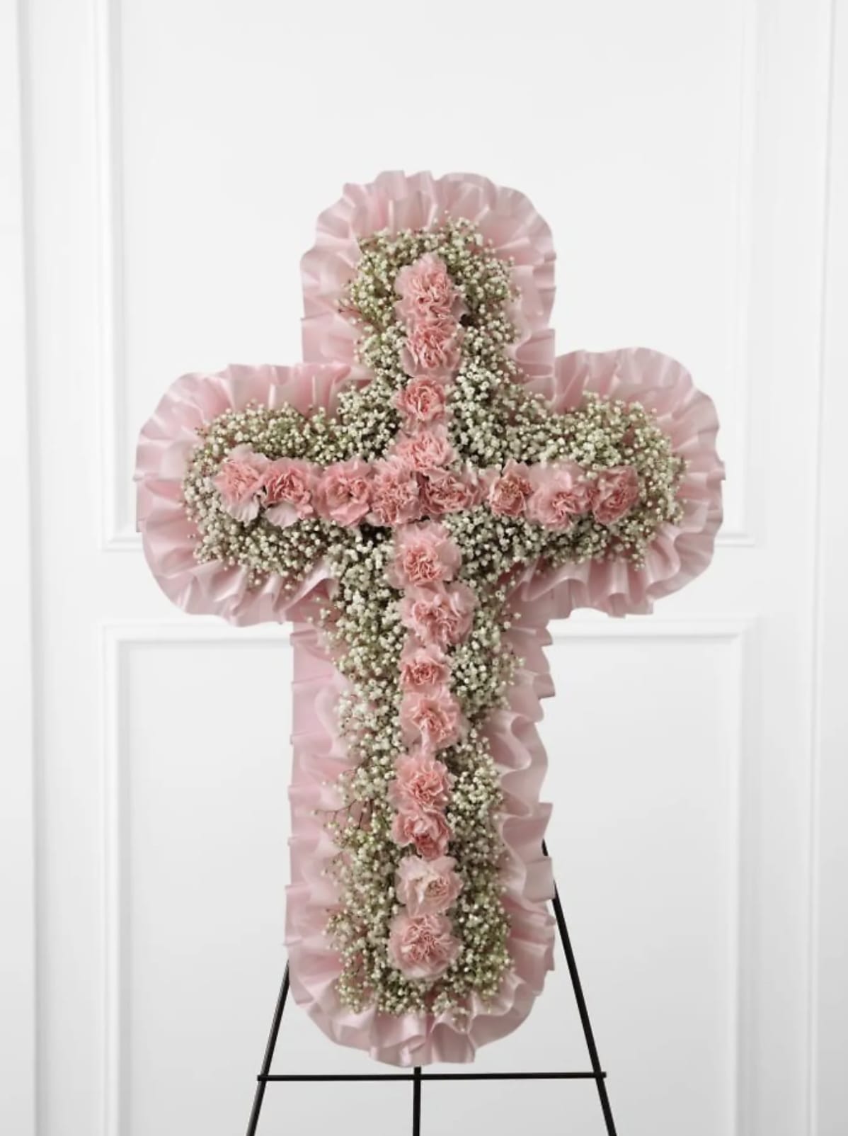 Heaven's Cross - The Heaven's Cross Easel is a graceful tribute to honor the life and faith of the deceased. Pink mini carnations and baby's breath are lovingly arranged in the shape of a cross accented with a pink satin ribbon around the outside and displayed on a wire easel to create a wonderful way to express your love for the departed.