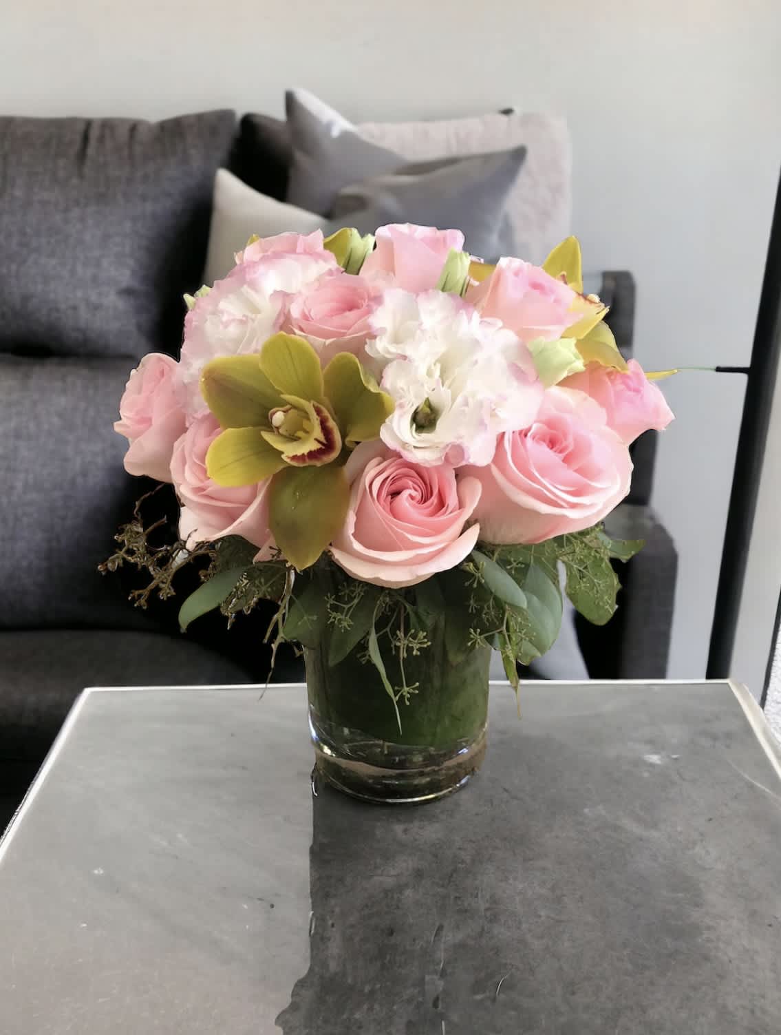 Pink cutie  - Flower : Pink roses, pink Lisianthus, green cymbidium, eucalyptus  Vase : 5” by 4” glass vase lined with ti leaf.