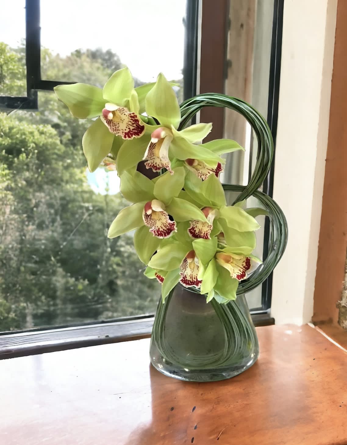 Number 8 cymbidium  - Flower : Green cymbidium orchids in a cylinder glass vase with  green steel grass designed  Vase : 6” by 5”