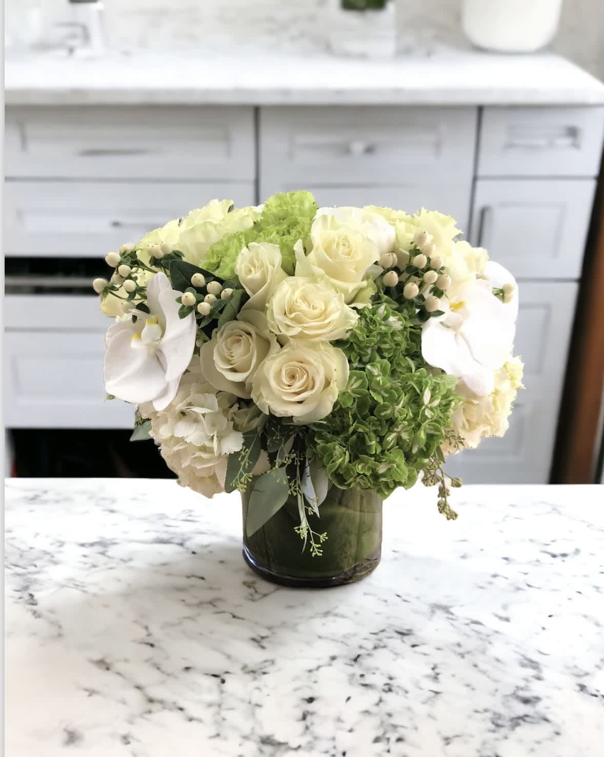 Green apple  - Flower : green hydrangeas, White hydrangeas, white roses. White coffee beans, White phalaenopsis orchids, Eucalyptus  Vase : A ti leaf lined 6 by 6 glass vase.