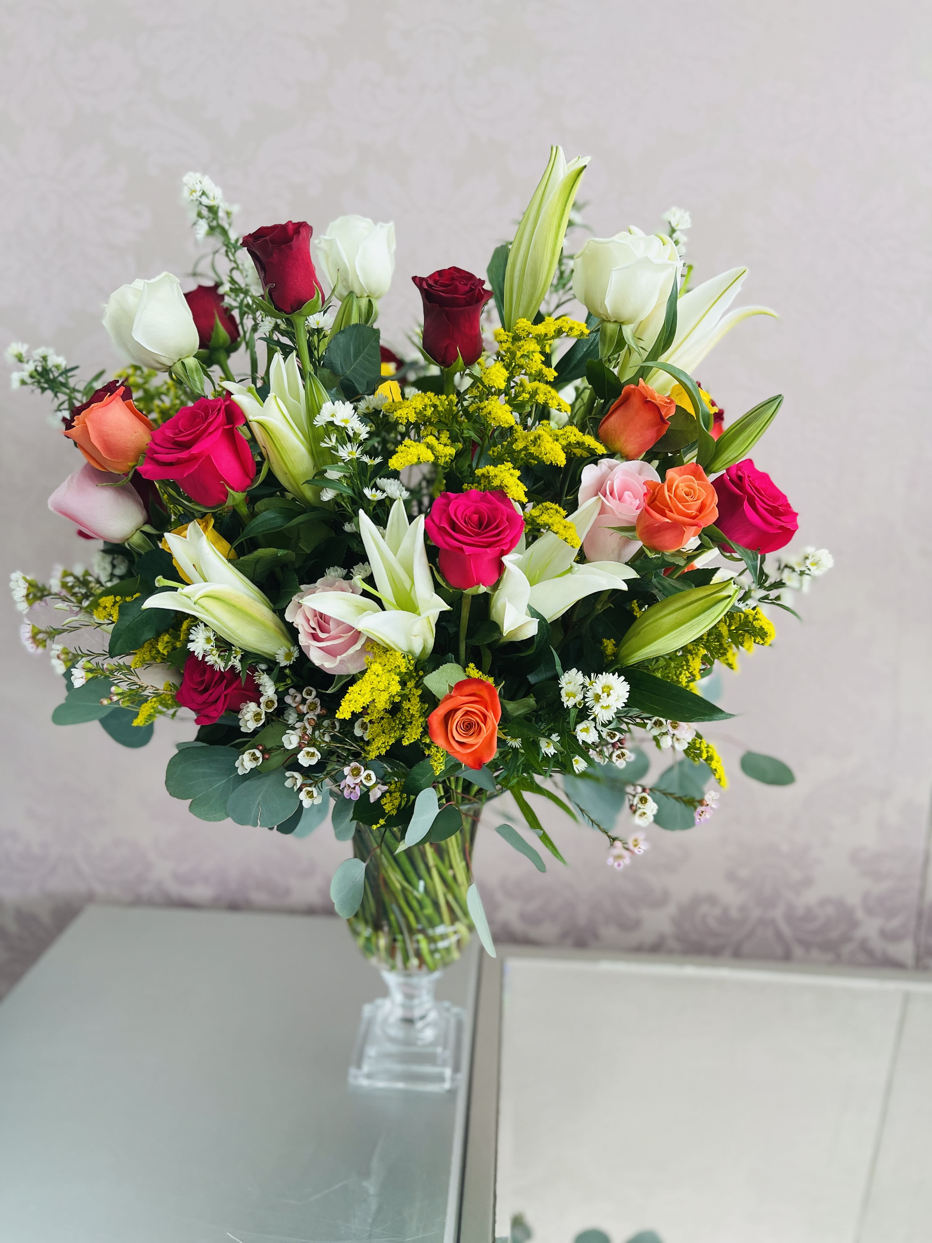 Rainbow Bouquet  - This colorful bouquet includes white lilies, roses , white aster , yelllow aster ,silver dollar eucalyptus, seeded eucalyptus, and lemon leaf. Delivered in a clear urn vase 