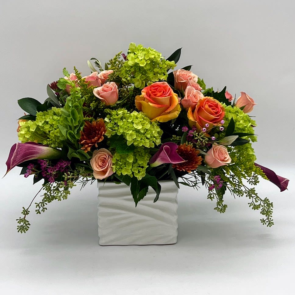 Sunset over the Mountains  - a perfect view from the comfort of your own home! natures beauty is truly magical. A beautiful arrangement adorned with Mini Green Hydrangeas arranged with peach spray roses, oranges roses and burgundy mini calla lilies in a white ceramic vase. 