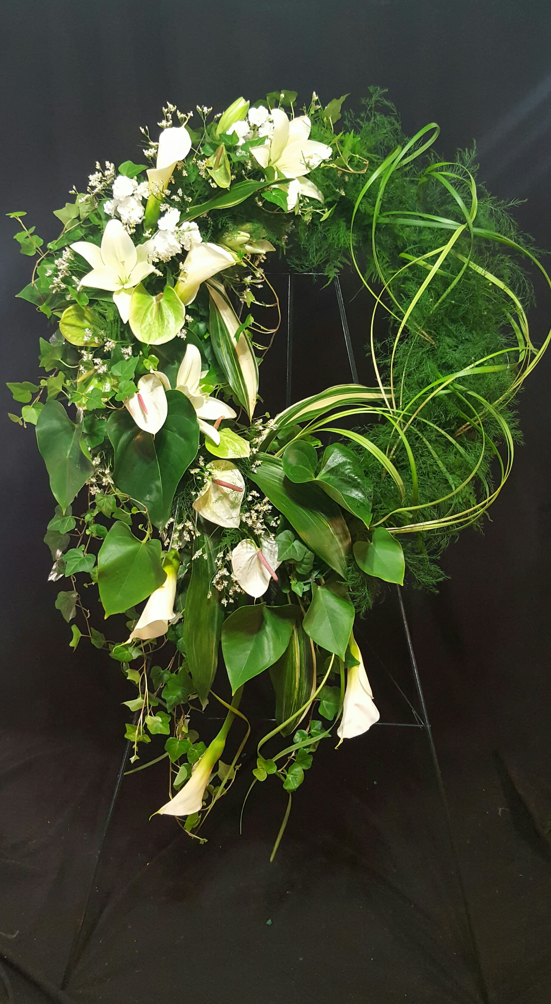 Serene Sympathy Wreath  - Finding the words to express your feelings during this difficult time can be challenging. Flowers help to express what we could never say. Send this artistic Green and White Tribute to express your condolences of the dearly departed. Hand Crafted by our florist with a mixture of foliage, Calla Lilies, Lilies, and Anthurium. 