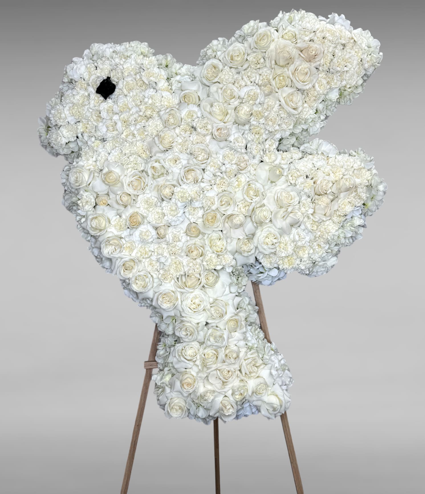 Eternal Affection  - Their pure heart and peaceful spirit will live on in a gesture symbolizing the dove of eternal life. Our standing cross of soothing florals, expertly crafted by our florists for a lush, full presentation, is a grand expression of your condolences, offering hope and serenity during a difficult time. All-white standing dove arrangement with white roses and white carnations.