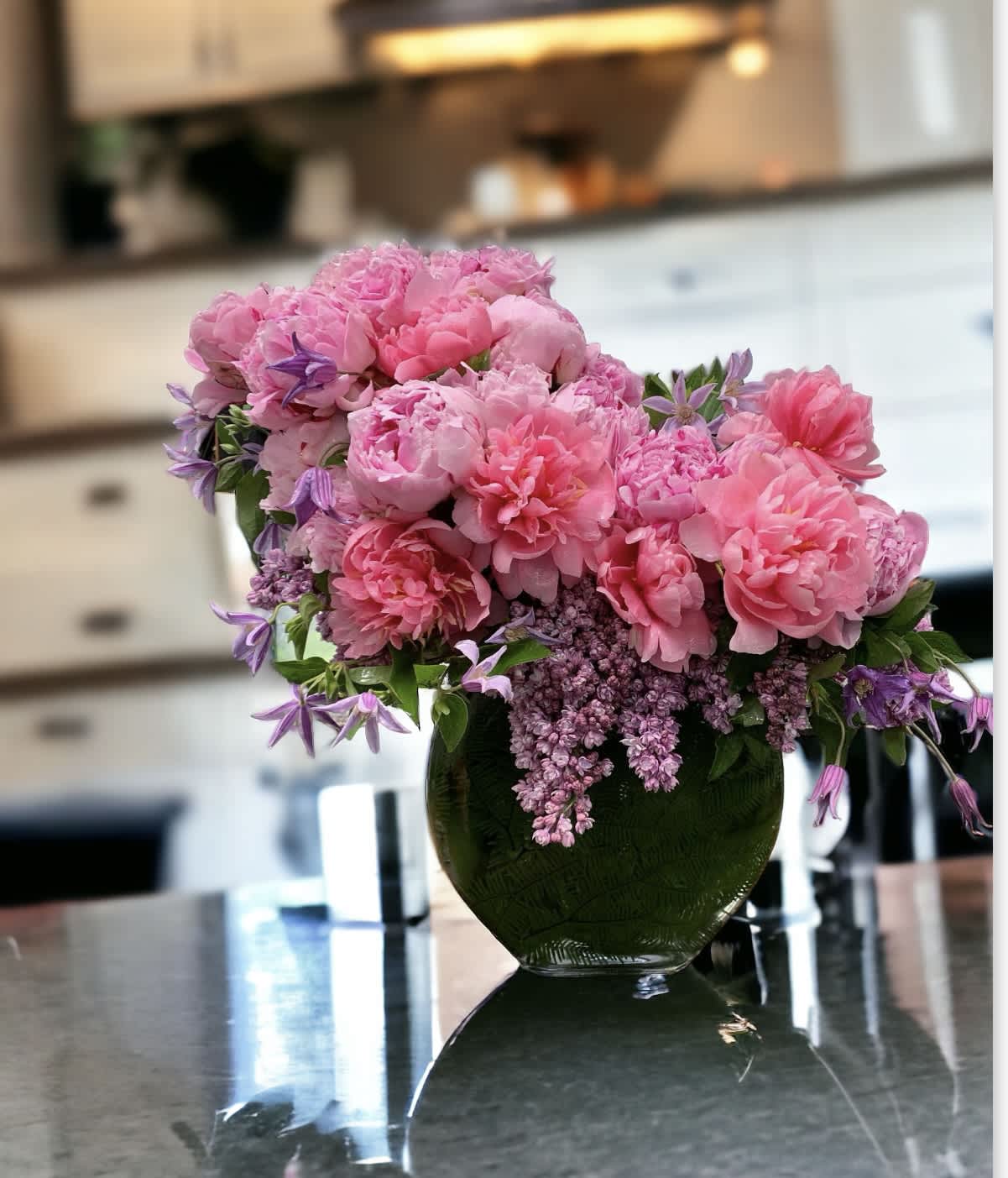 Oh! Peonies Oh! Peonies - A medley of pink peonies, meet whimsical tulips, lavender lilacs, clematis Resting inside a 7” x 7” clear helf moon vase, the arrangement stands overall 14” tall and 16”wide.