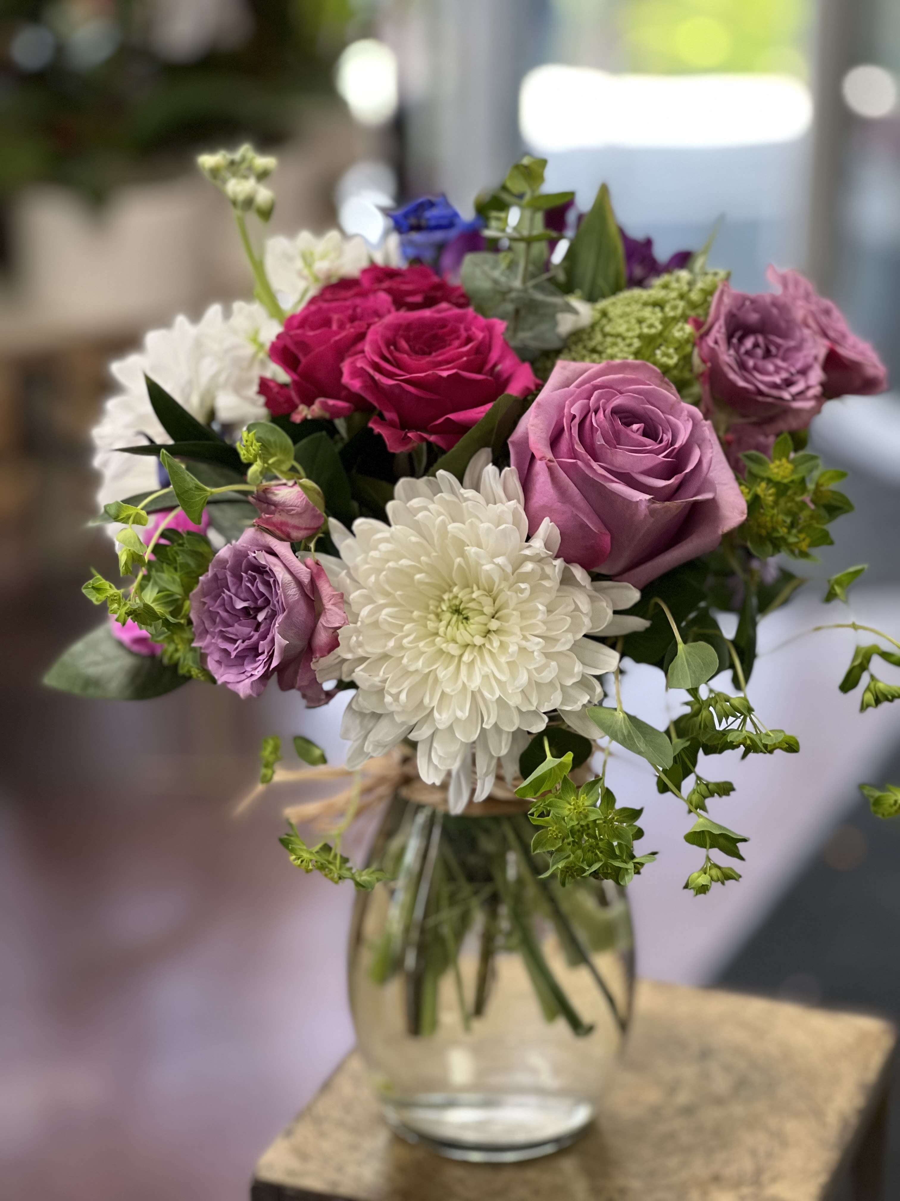 Happy petals bouquet by Charlene Happy petals bouquet by Charlene - Mixture of a seasonal flowers, including purple roses arranged in clear glass vase With a raffia decoration