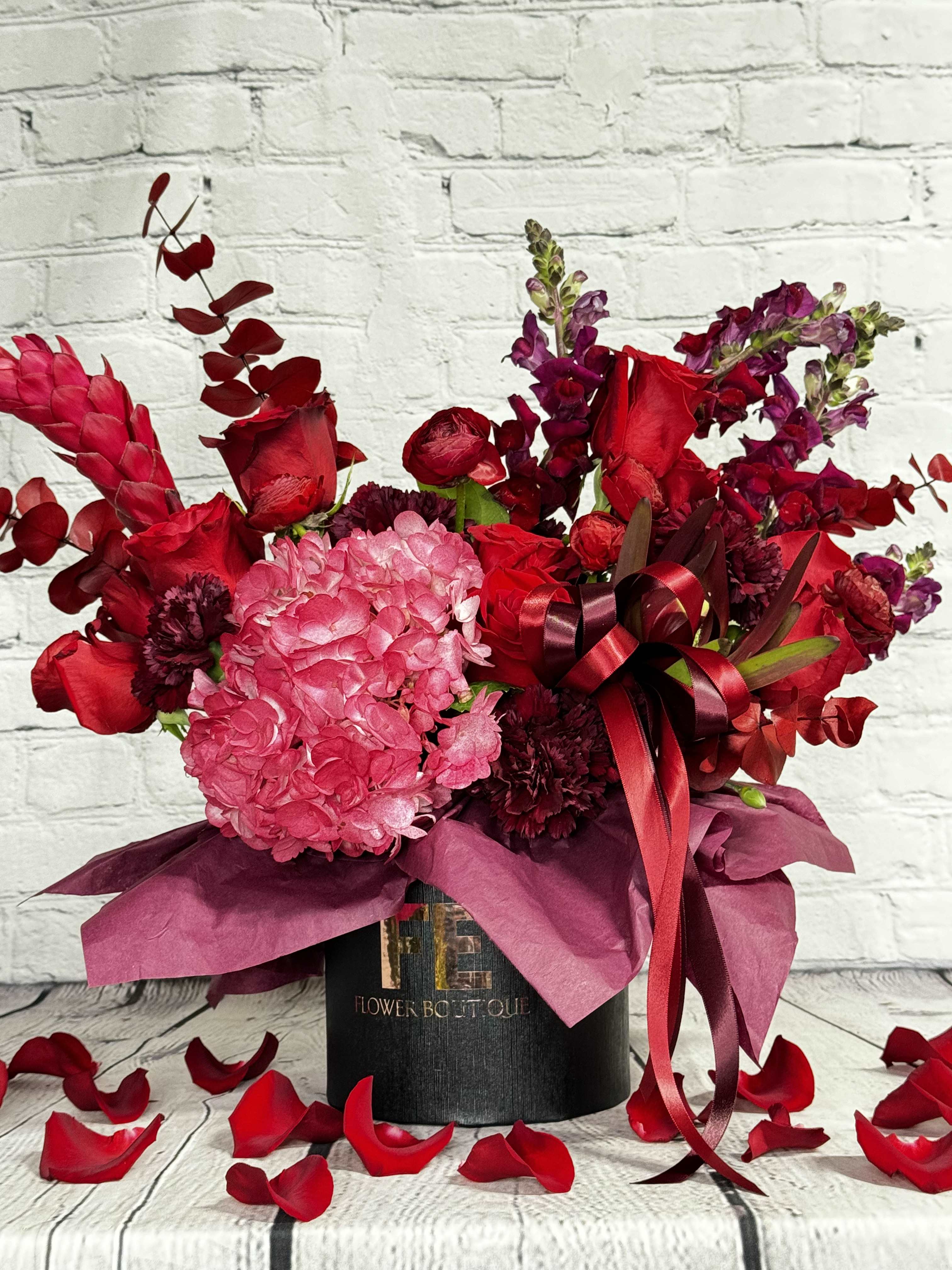 Dark Romance - Indulge in a world of enchantment with our &quot;Dark Romance&quot; floral arrangement, a luxurious display of rich burgundy hues that will leave you breathless. The bouquet features deep red roses, elegant red ranunculus, classic red carnations, bold red snapdragons, beautiful red hydrangea, exotic red ginger, and luxurious burgundy eucalyptus.  The black box serves as a striking and elegant base, making the rich reds of the flowers stand out even more. The deep and alluring burgundy hues create an atmosphere of excitement, seduction, and a unique sense of &quot;dark romance.&quot;   This bold and mesmerizing floral arrangement is perfect for those who seek a unique and luxurious touch in their interior decor or special event. The red and burgundy colors are sure to create a romantic atmosphere, whether you're celebrating a birthday, anniversary, or looking for a centerpiece for your wedding.  A unique blend of textures, shapes, sizes, and hues, this &quot;Dark Romance&quot; bouquet is a sensory experience that will leave you enchanted and wanting more. Order now and discover the beauty and power of true luxury floral arrangements!