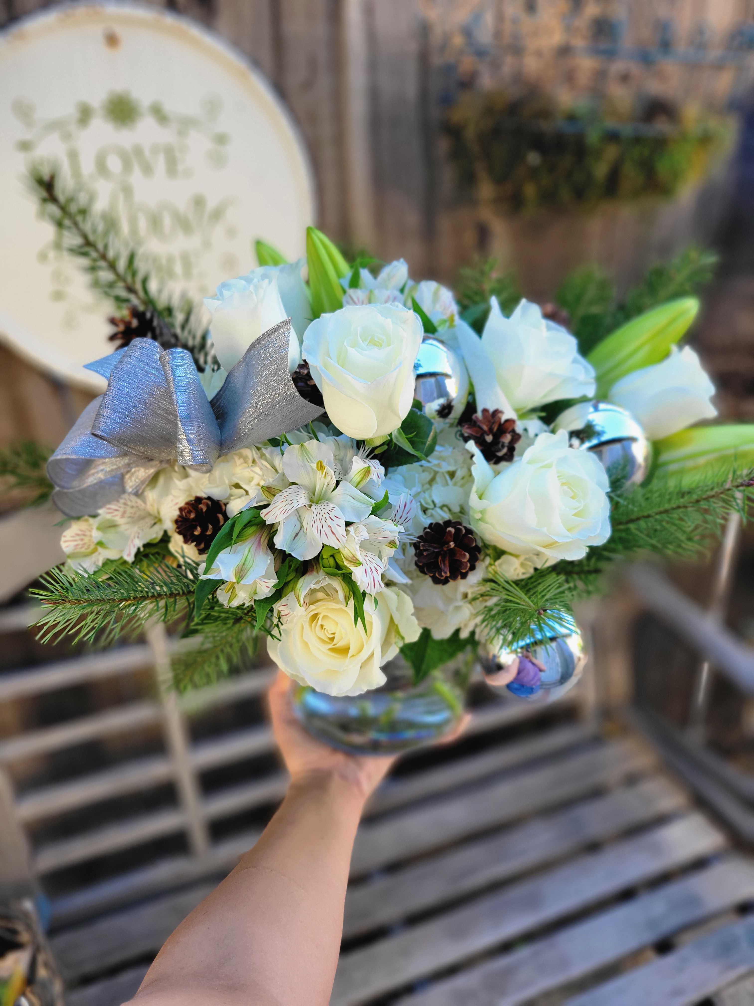 White Christmas - We are all dreaming of a white Christmas, make your loved one's dream come true with this darling Christmas exclusive. Featuring all white florals such as Roses, Hydrangea, Lilly. And Christmas themed accents such as Evergreens, Douglas Fir, &amp; Pine cones. Completed with Silver Christmas Ornaments and a Silver ribbon  We gladly deliver this item Nov - January!