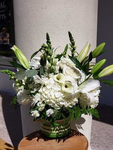 White Elegance - Introducing our exquisite White Elegance flower arrangement, a stunning composition of hydrangeas, roses, stock, and lilies artfully arranged in a clear glass cylinder vase. This elegant ensemble showcases the timeless beauty and elegance of white flowers, creating a captivating display that will leave anyone in awe.  The arrangement features delicate white hydrangeas, their voluminous blooms adding a sense of grace and sophistication to the composition. These breathtaking flowers symbolize heartfelt emotions and are often associated with abundance and gratitude.  Next, we have the classic and romantic white roses. Their velvety petals and intoxicating fragrance evoke feelings of love and admiration. These timeless blooms are carefully nestled among the other flowers, adding a touch of elegance and charm.  The fragrant white stock adds a layer of texture and depth to the arrangement. These beautiful flowers with their tall stems and clustered blooms emit a delightful, sweet fragrance that fills the room, creating a truly sensory experience.  Completing this majestic combination are the elegant white lilies. Their trumpet-like blooms and stunning white petals exude purity and innocence. These flowers are known to represent devotion and are a symbol of both beauty and serenity.  Each flower is hand-selected and expertly arranged in a clear glass cylinder vase, allowing the natural beauty of the flowers to shine. The transparent vase adds a modern touch and allows for a clear view of the meticulously arranged flowers, creating a breathtaking focal point.  Our all-white flower arrangement is perfect for any occasion, whether it be a wedding, anniversary, or simply to bring a touch of elegance to your home or office space. It also makes a thoughtful gift for someone special, conveying a feeling of purity, love, and appreciation.  Experience the timeless beauty and serenity of our all-white flower arrangement. Place your order today to bring the delicate charm and enchanting ambiance of white flowers into your life or to surprise a loved one with a truly breathtaking gift. 