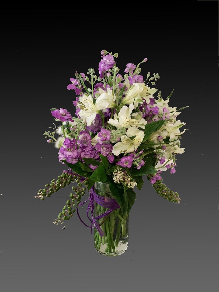 Jumping for Joy - Send her on a dreamy stroll through a garden with this perfect-for-any-occasion bouquet. Soft lavender and pink flowers delight with a sweet smell; a pink ribbon adds to the feminine look of this traditional arrangement. Lush lavender stock, pale pink alstroemeria, hot pink spray roses and mini carnations are delivered in a traditional glass vase.