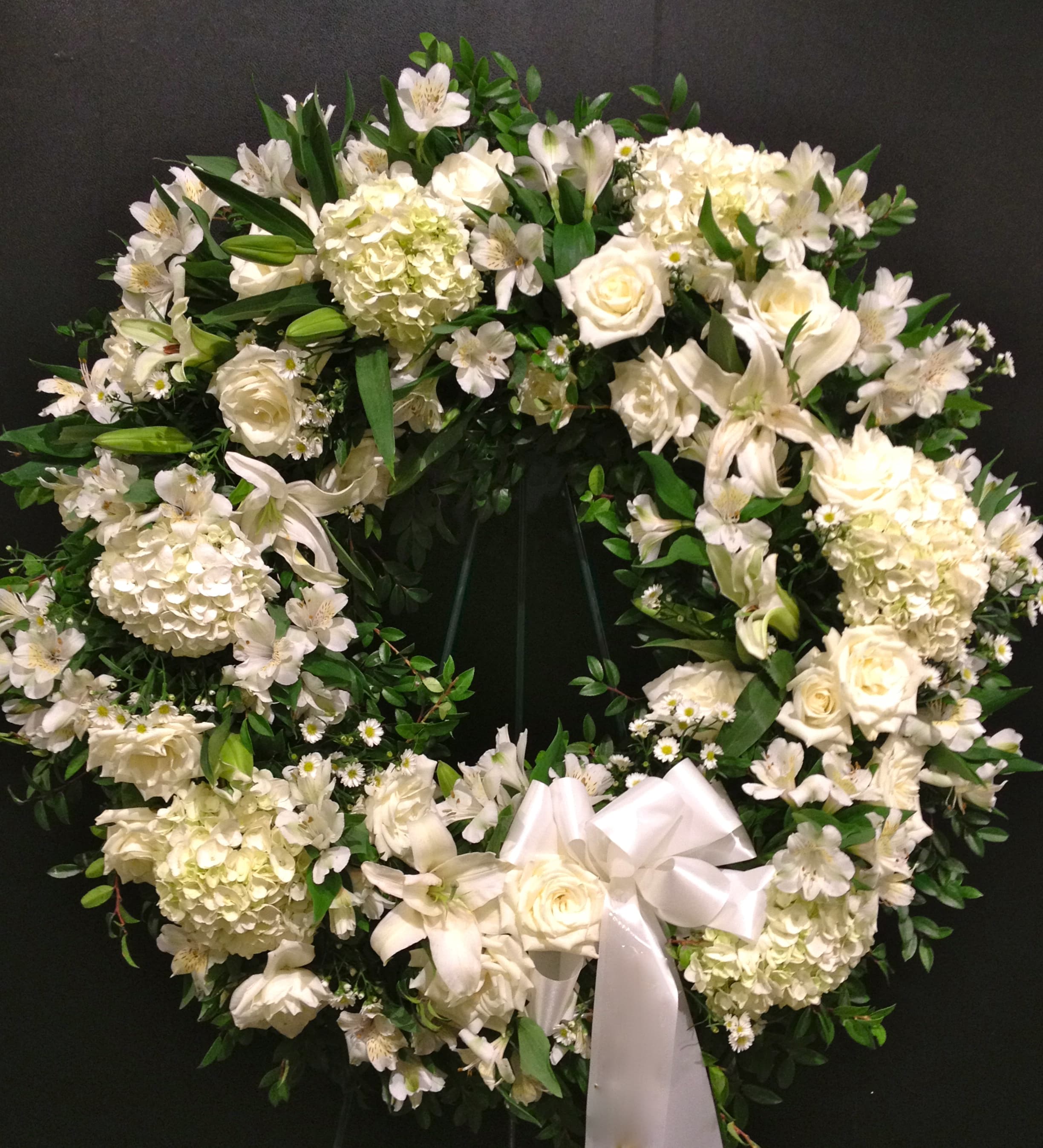 All White Wreath - A pure and delicate expression of adoration. This wreath of whites gently embraces loving memories, and offers solace and sweet thoughts at a time of loss. Lovely blooms such as White Roses, White Hydrangea, White Lilies and White Alstroemeria are nestled together and accented with White Monte Casino. 