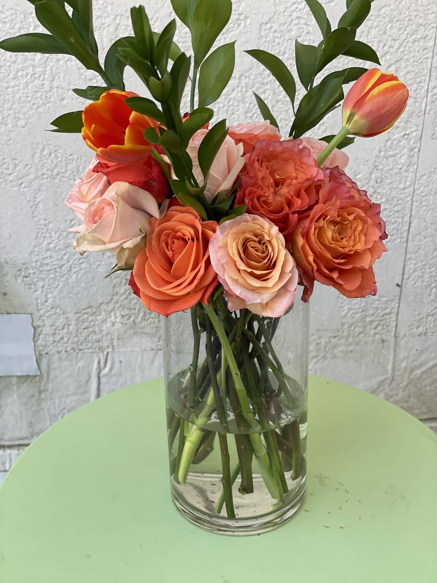 Orange Elegance - This arrangement is a beautiful combination of garden roses,tulips, and roses in tones of orange and peach, paired with stately Ruscus leaves.